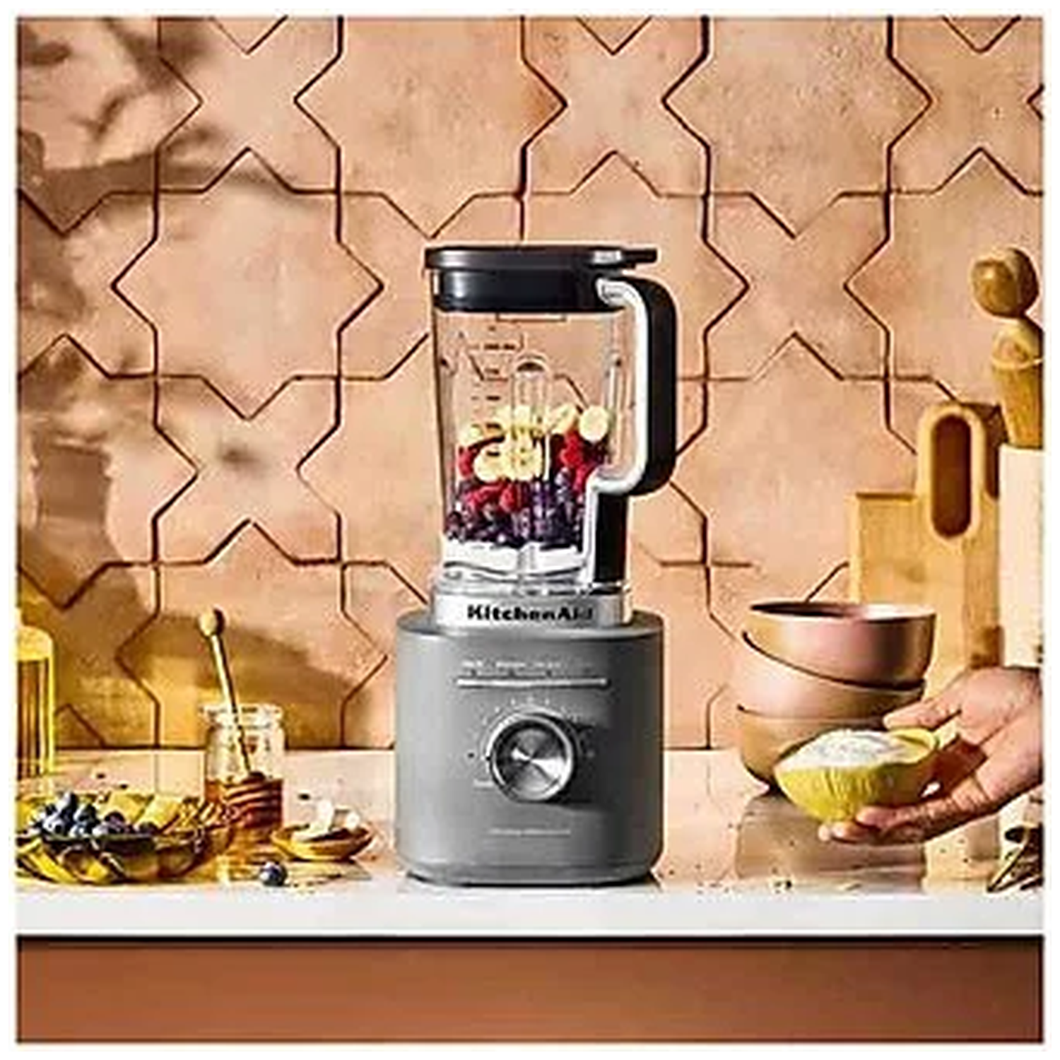 Gray blender with fruit, next to bowls of honey and berries.