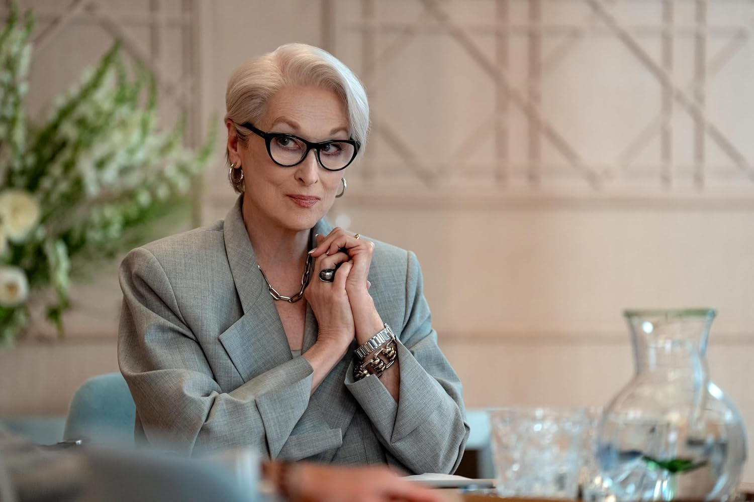 Eine ältere Frau mit grauem Haar und Brille trägt einen grauen Blazer.