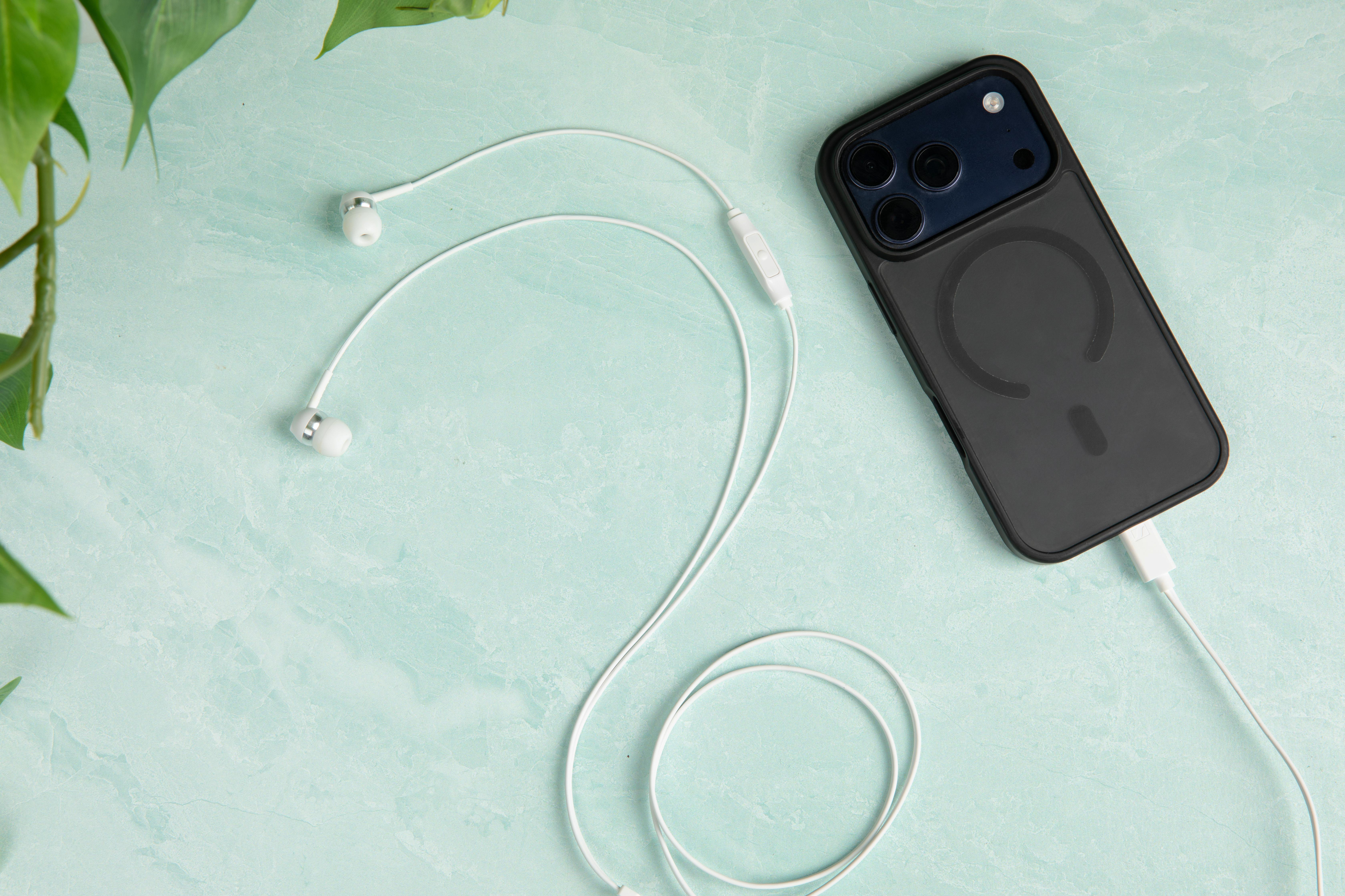 Weiße Kopfhörer liegen neben einem schwarzen iPhone mit Ladekabel auf blauem Hintergrund.