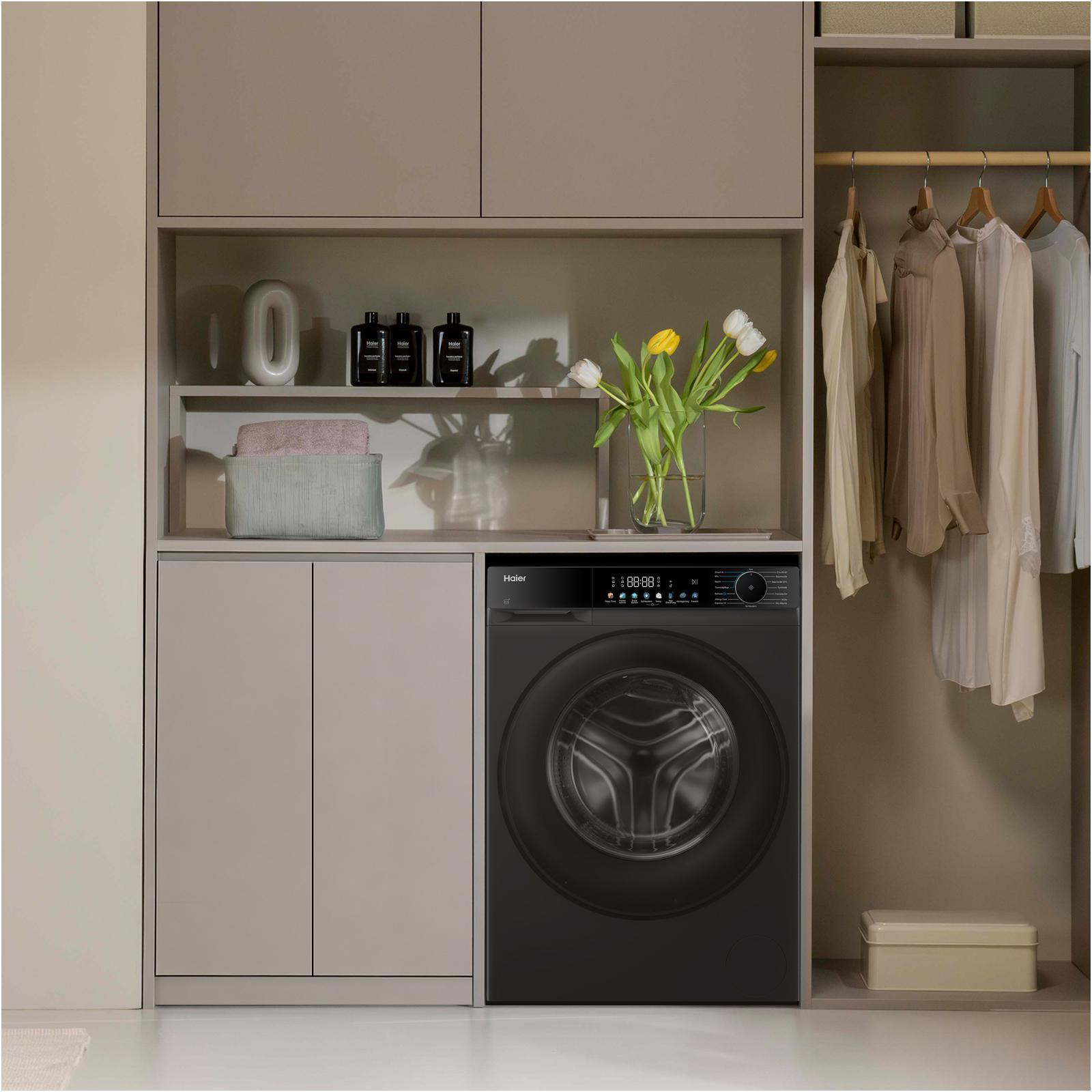 Eine schwarze Haier-Waschmaschine steht neben einem Kleiderschrank mit Kleidung.