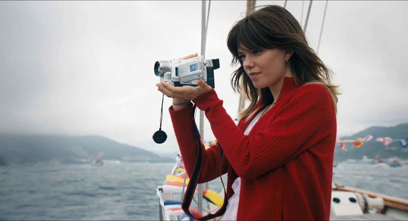 Eine Frau filmt mit einem Camcorder auf einem Boot, im Hintergrund sind Boote und Berge.