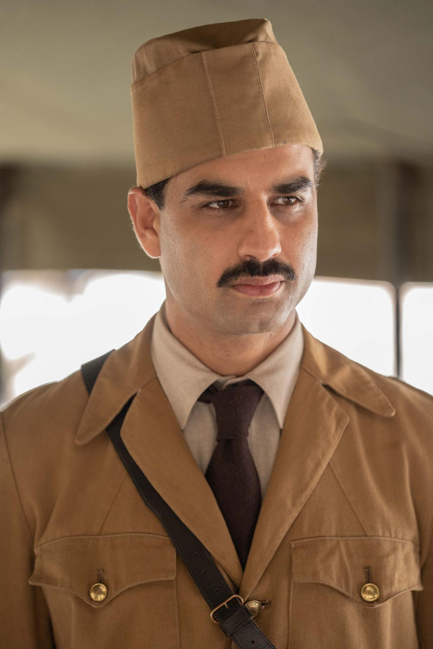 Ein Mann mit Schnurrbart trägt eine braune Uniform und einen braunen Hut.