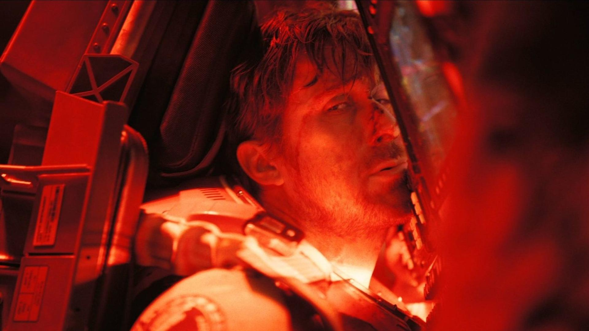Ein Mann mit blutigem Gesicht sitzt in einem roten Cockpit, sein Blick ist abwesend.