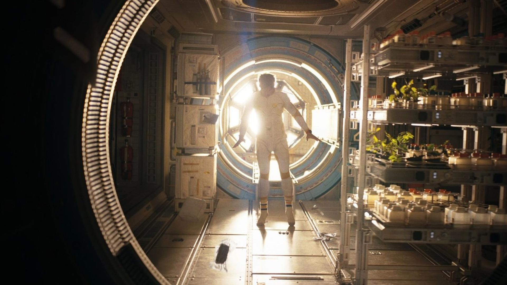 Ein Astronaut in einem weißen Anzug steht in einem Raumschiff vor einem runden Fenster.