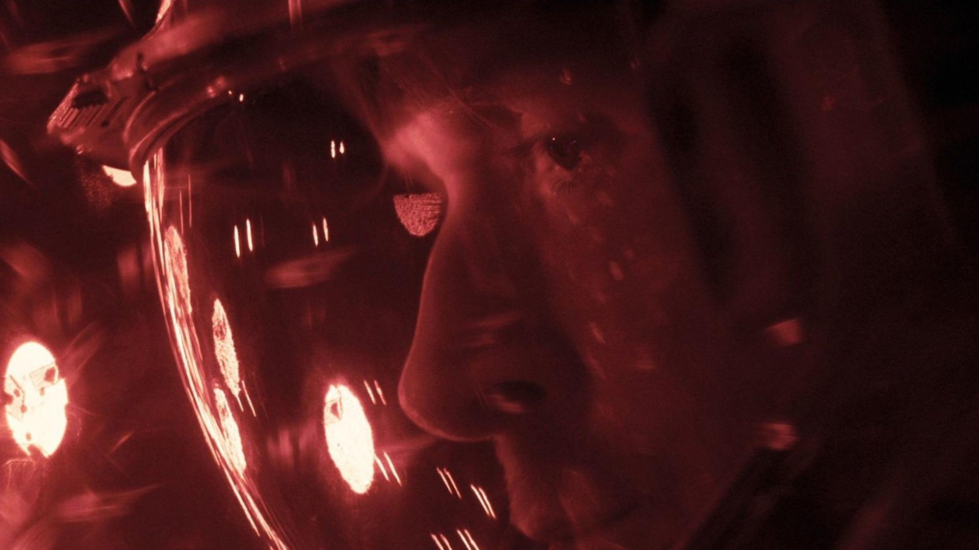 Nahaufnahme einer Person in einem rot beleuchteten Helm, Lichter spiegelnd.