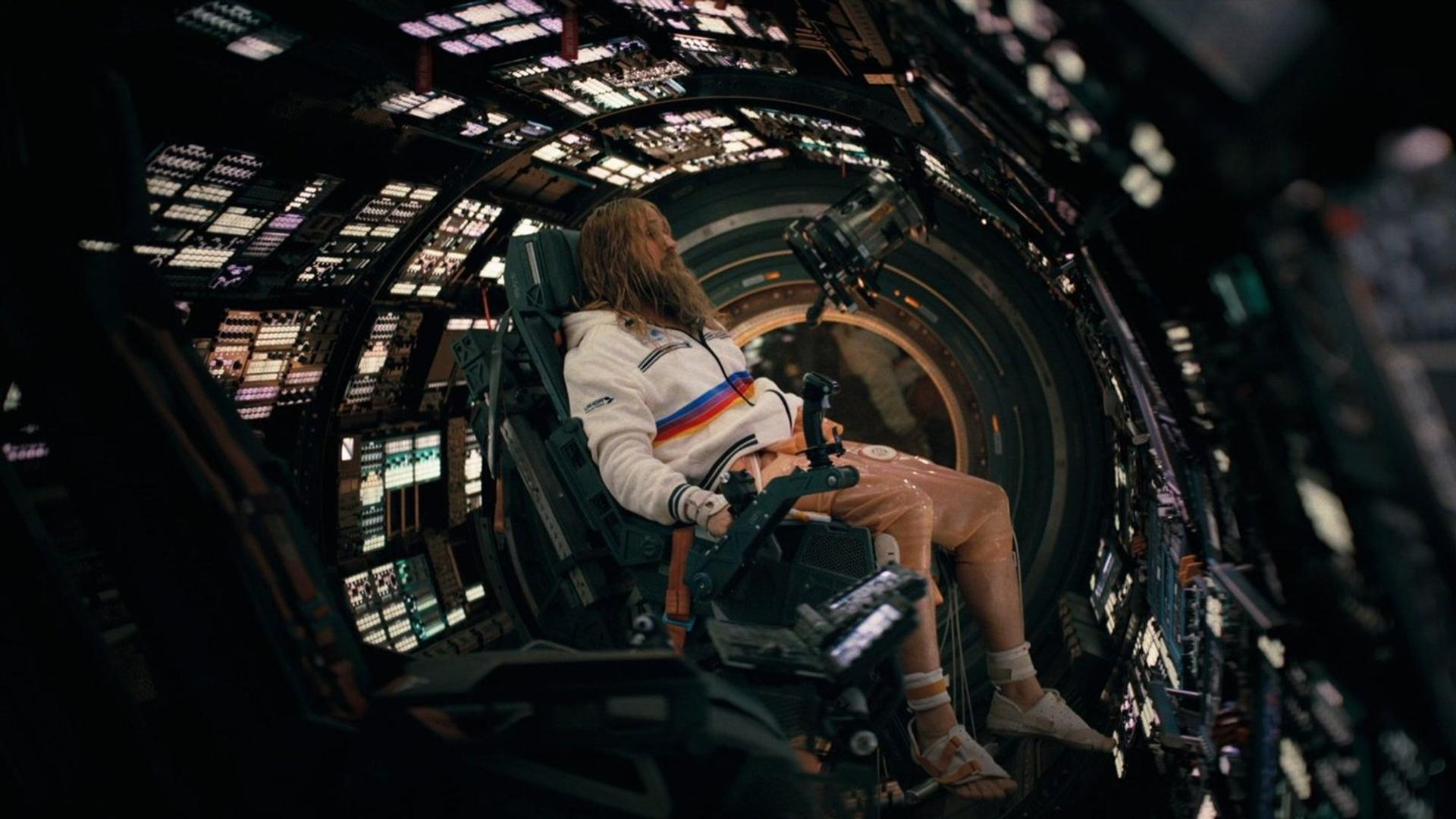 Mann mit Bart sitzt in einem Raumschiff-Cockpit mit vielen Lichtern und Bildschirmen.