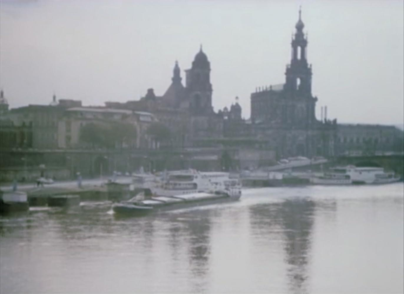 Schiff auf einem Fluss mit einer Stadtsilhouette und Kirchtürmen im Hintergrund.
