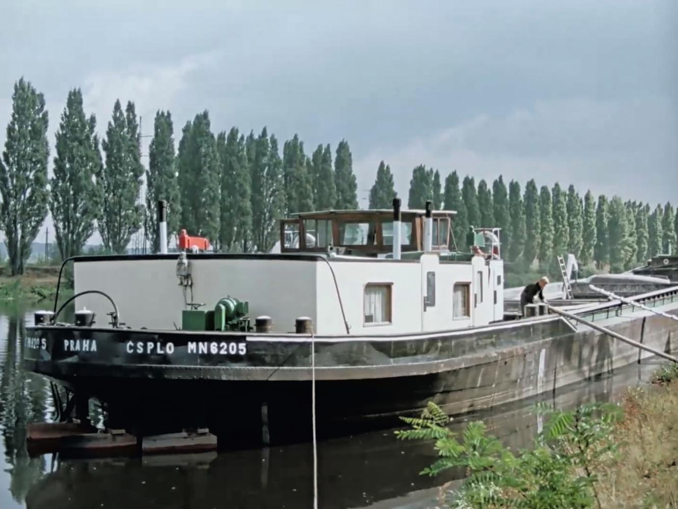 Ein weiß-schwarzer Kahn namens CSPLO MN6205 fährt auf einem Kanal an hohen Bäumen vorbei.