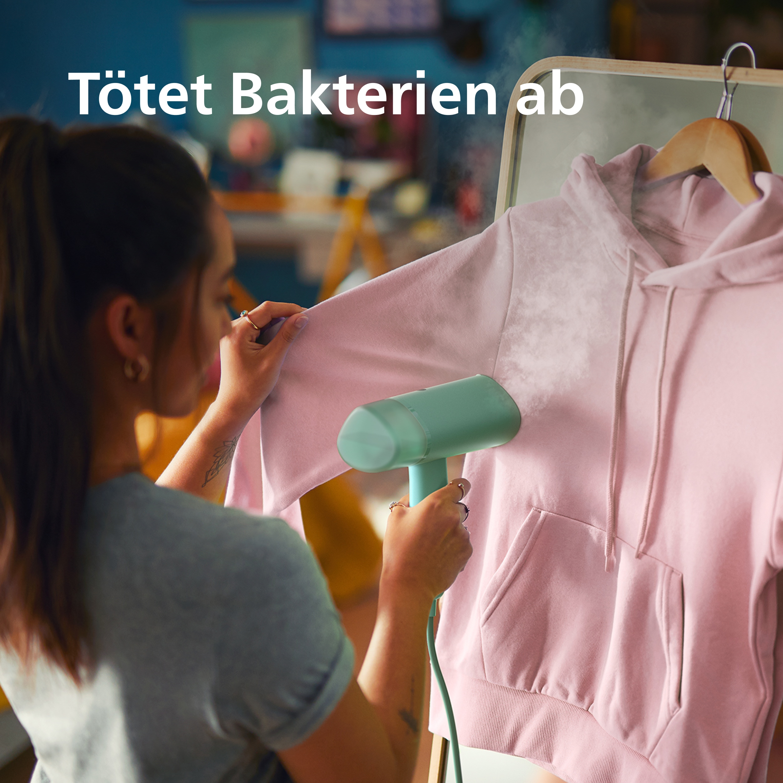 Eine Frau glättet einen rosa Hoodie mit einem Handdampfer. Dampf steigt auf.