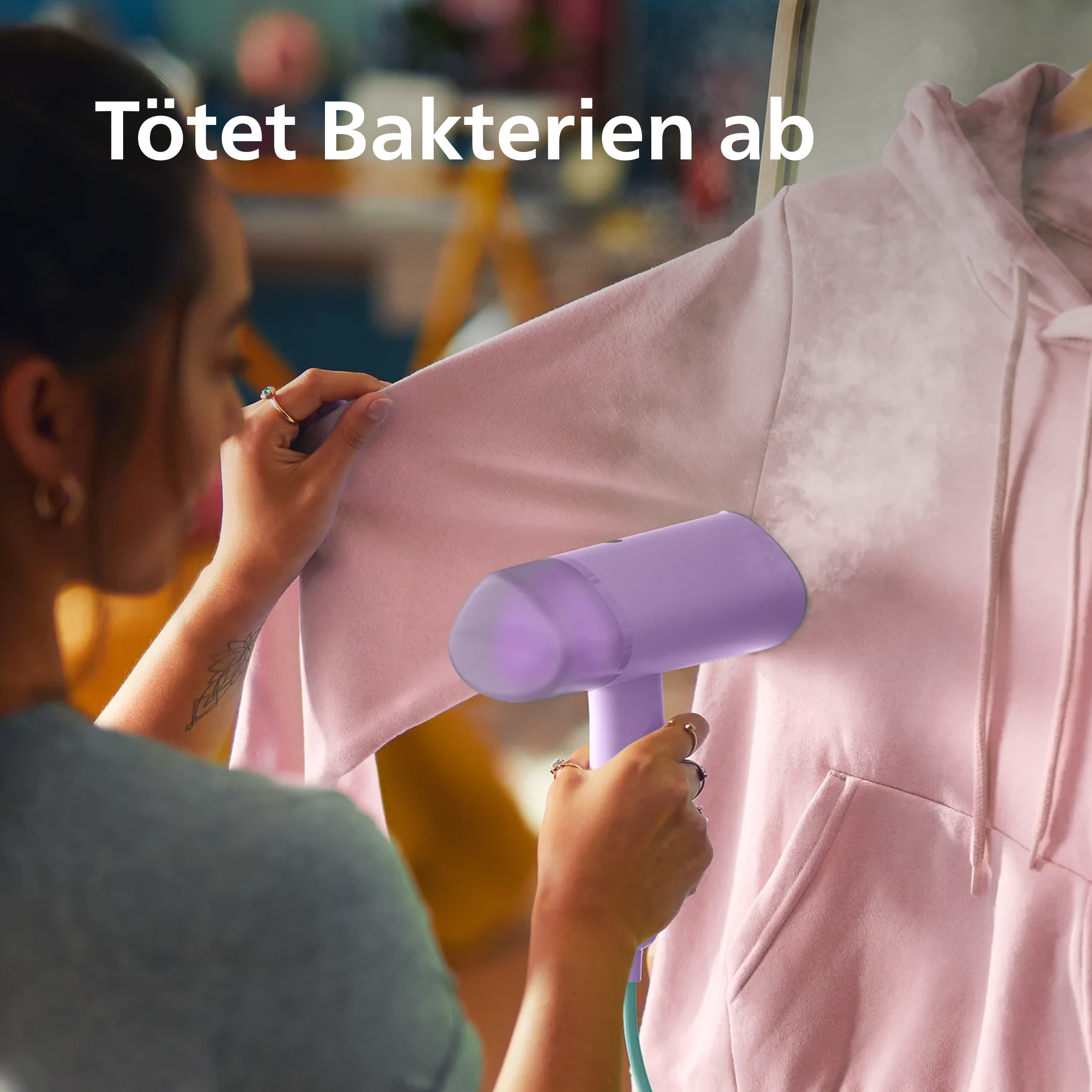 Eine Person glättet ein rosafarbenes Sweatshirt mit einem lila Dampfglätter.