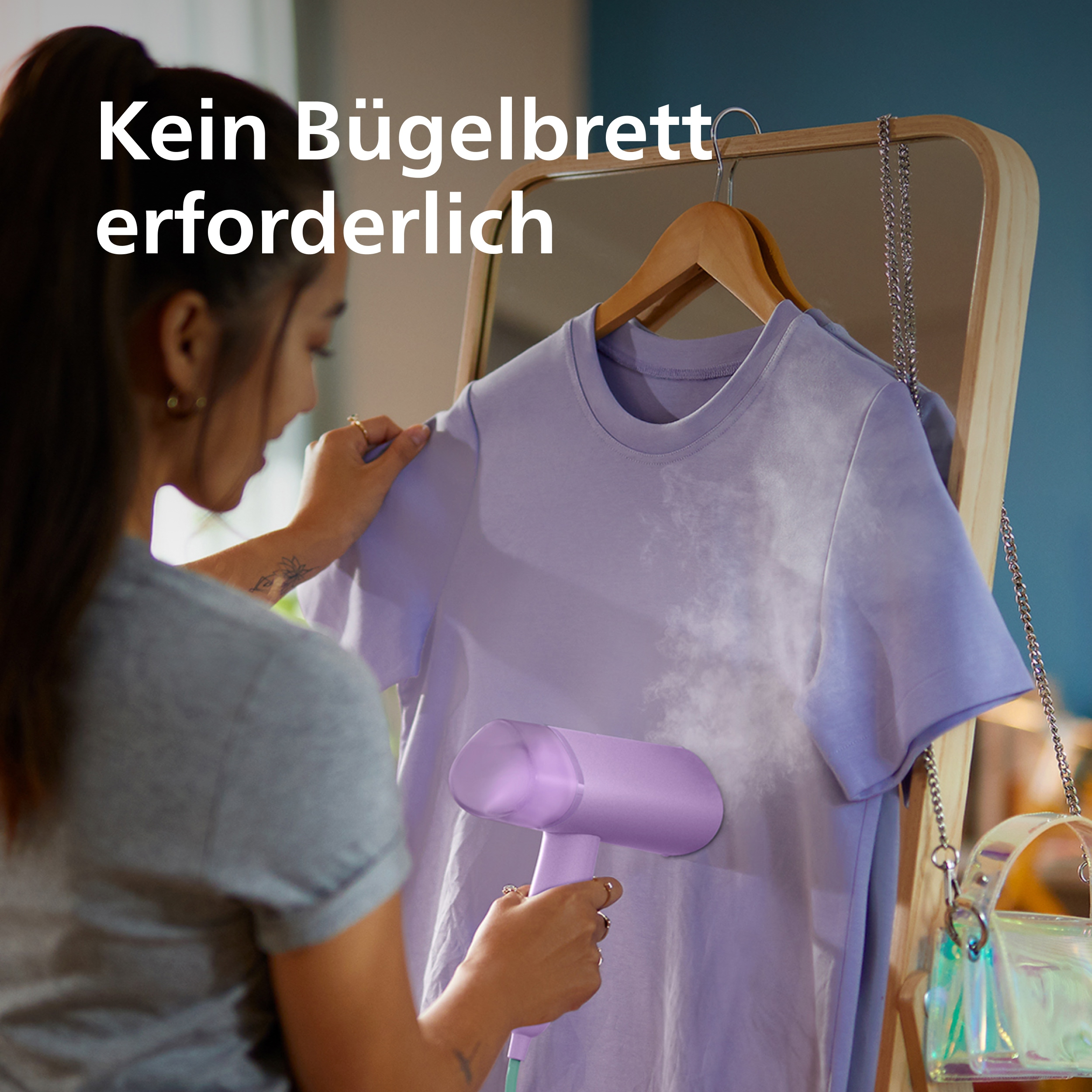Eine Frau glättet ein lila T-Shirt mit einem Handdampfer vor einem Spiegel.