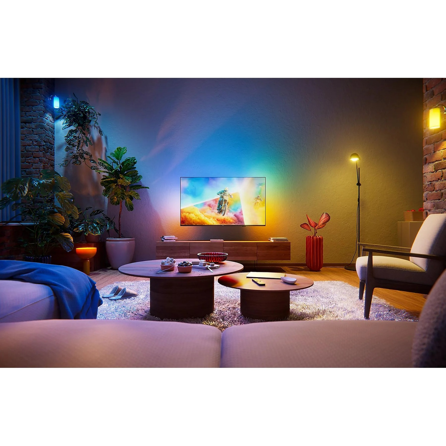 Living room with TV showing motocross, colorful lights, plants, and furniture.