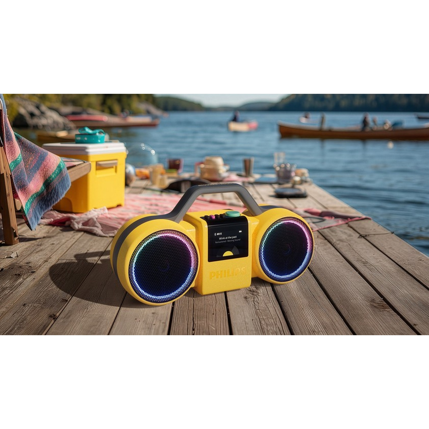 Altoparlante Bluetooth giallo con luci su un molo di legno vicino a un lago. Barche sullo sfondo.