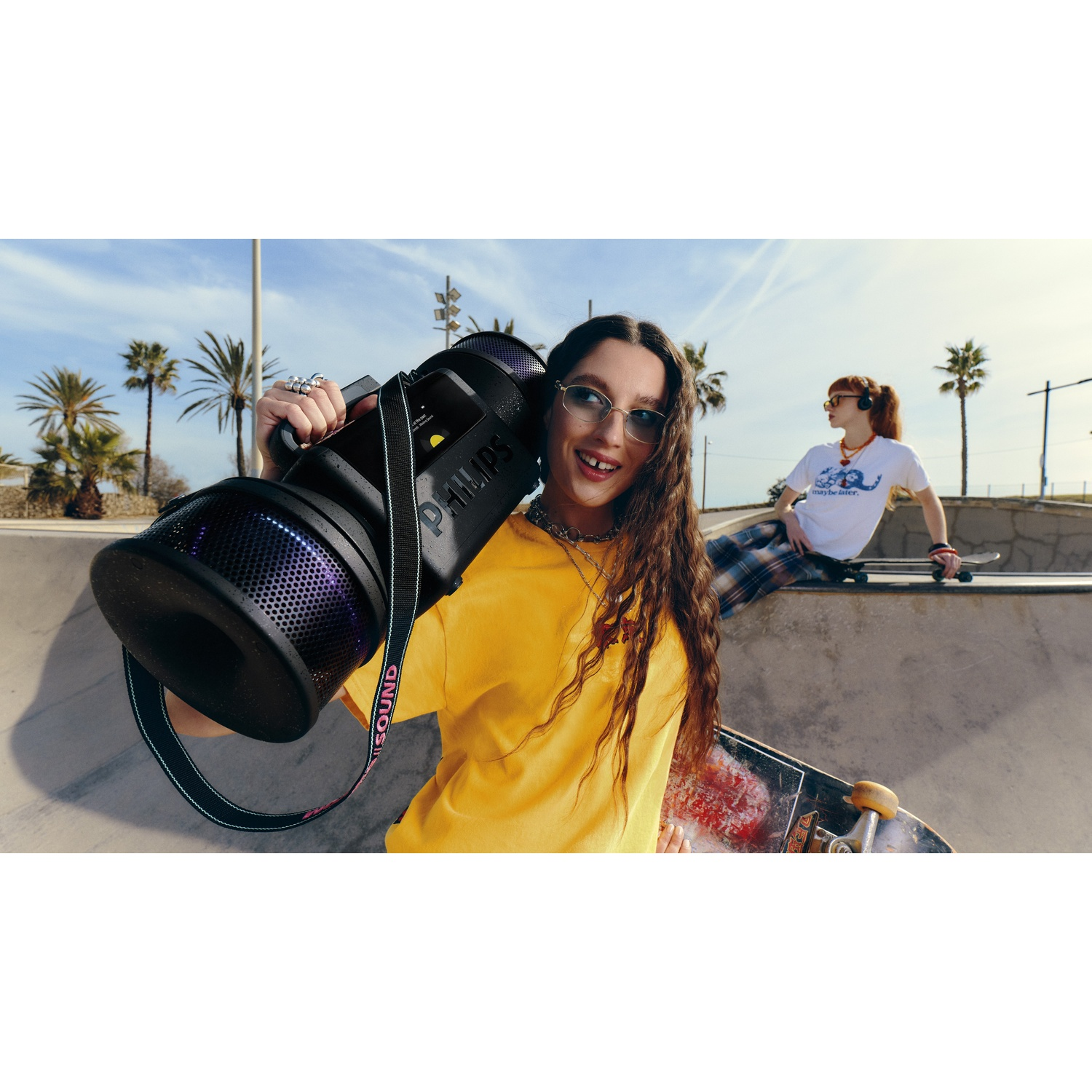 Donna con altoparlante nello skatepark, amica sullo sfondo con skateboard.