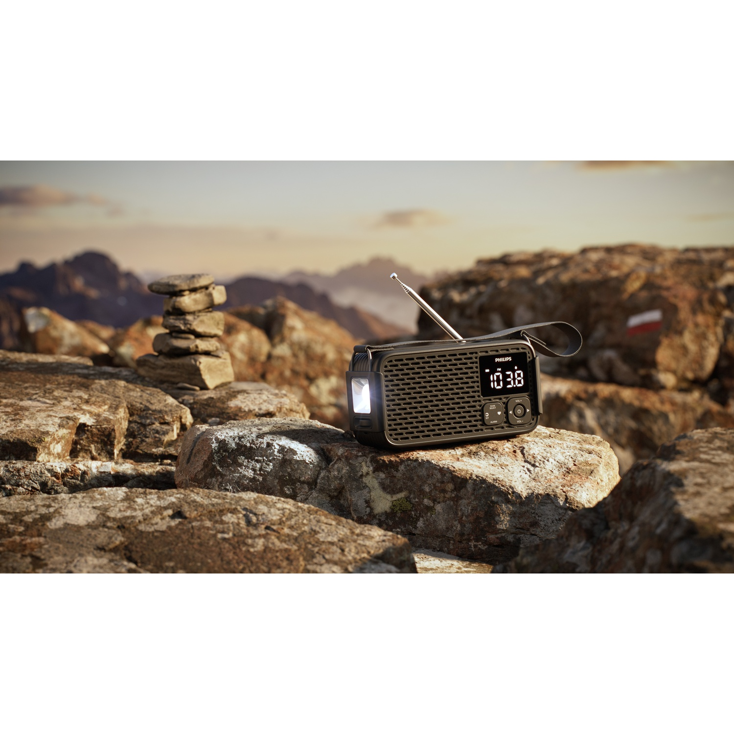 Una radio Philips nera con display illuminato si trova su rocce in un paesaggio montano al tramonto.