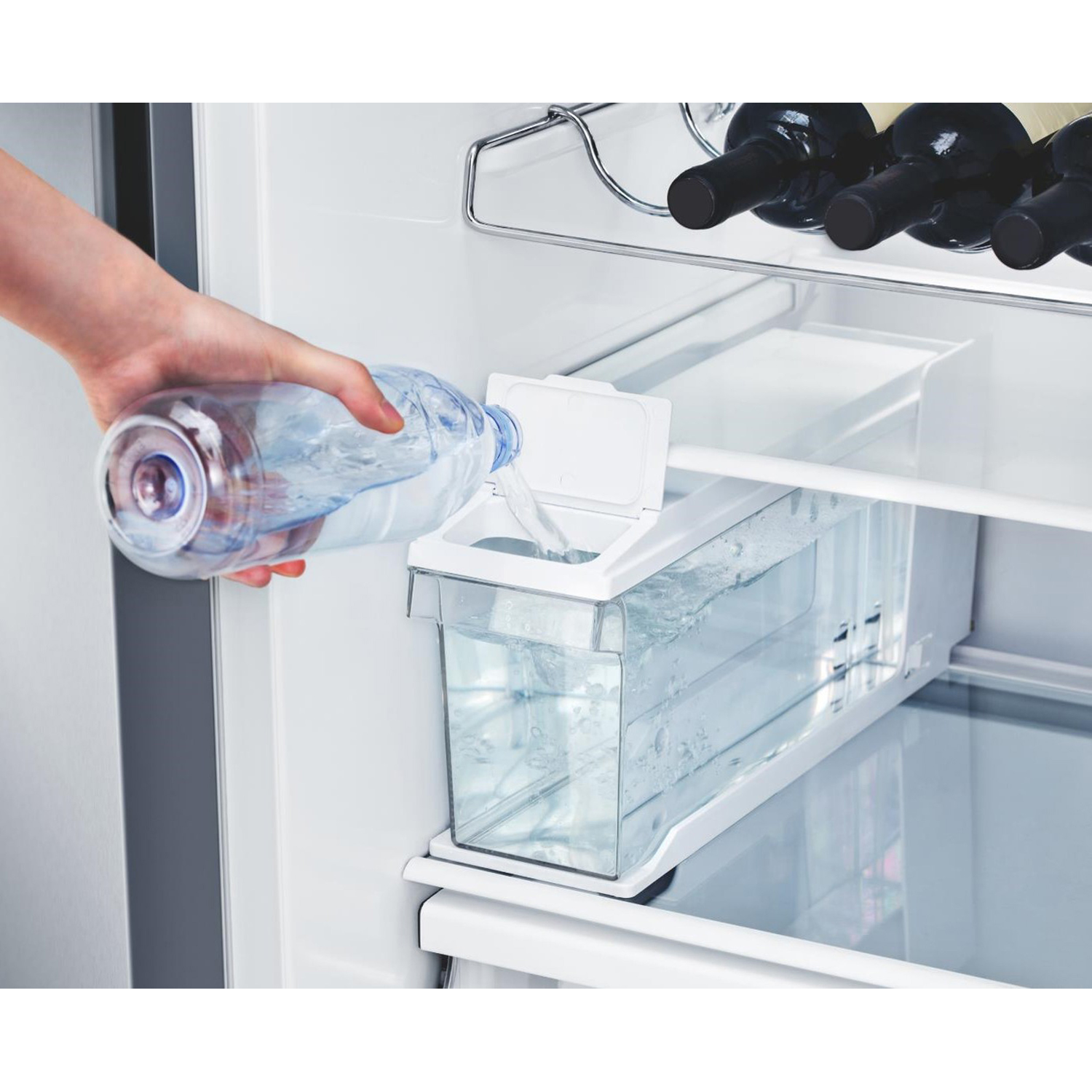 Een hand giet water uit een fles in een koelkastvak.