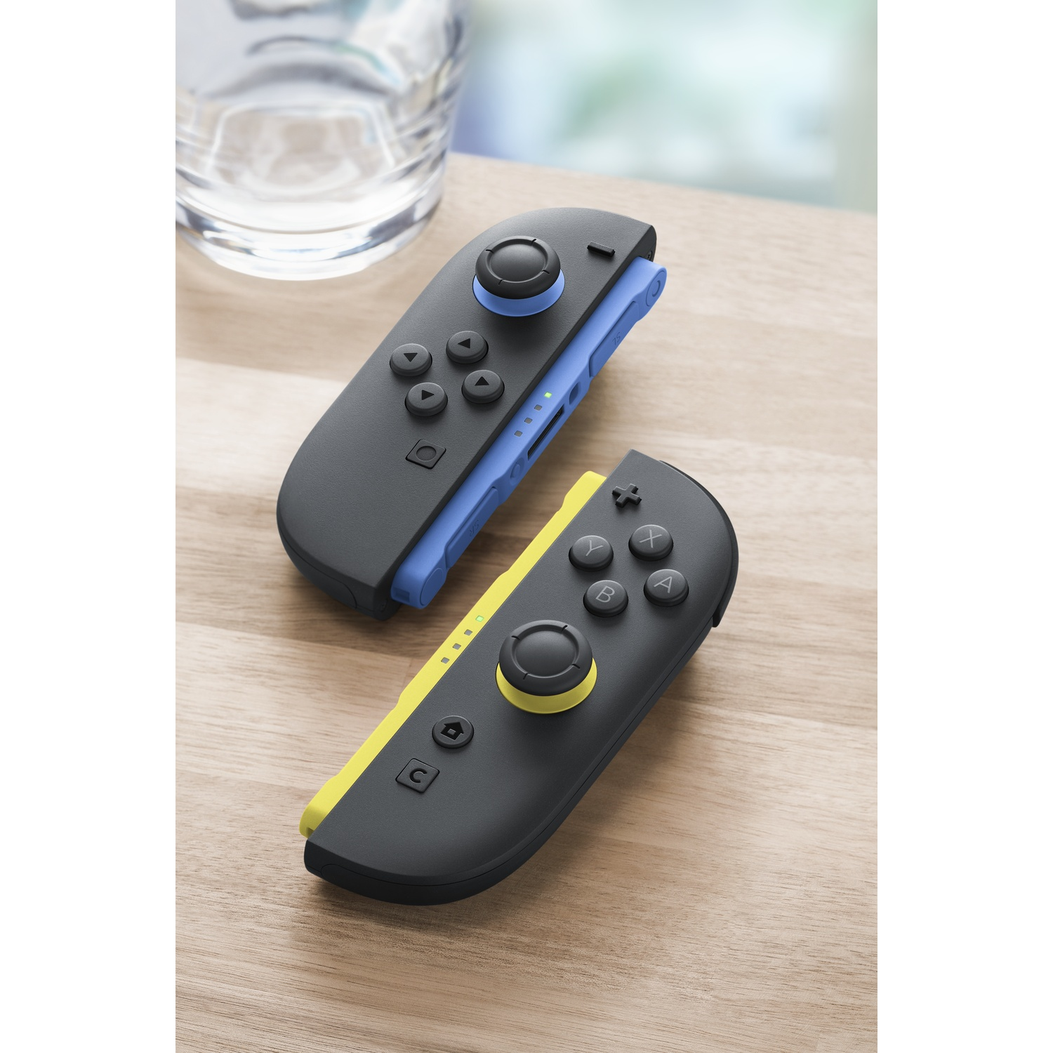 Two game controllers, one blue and one yellow, rest on a wooden surface.