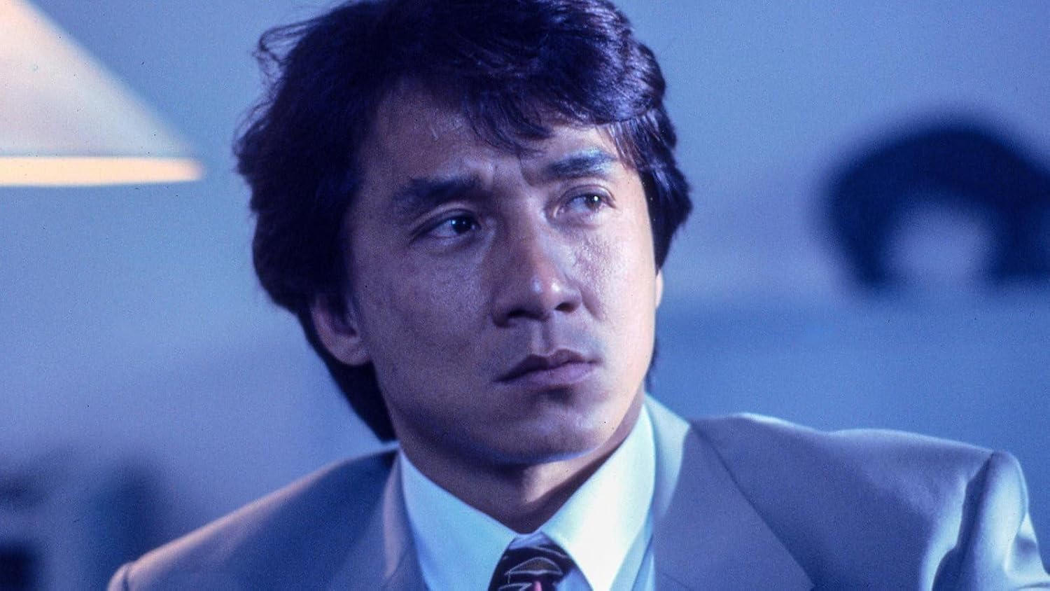 Jackie Chan in einem grauen Anzug und weißem Hemd mit Krawatte schaut nach rechts.