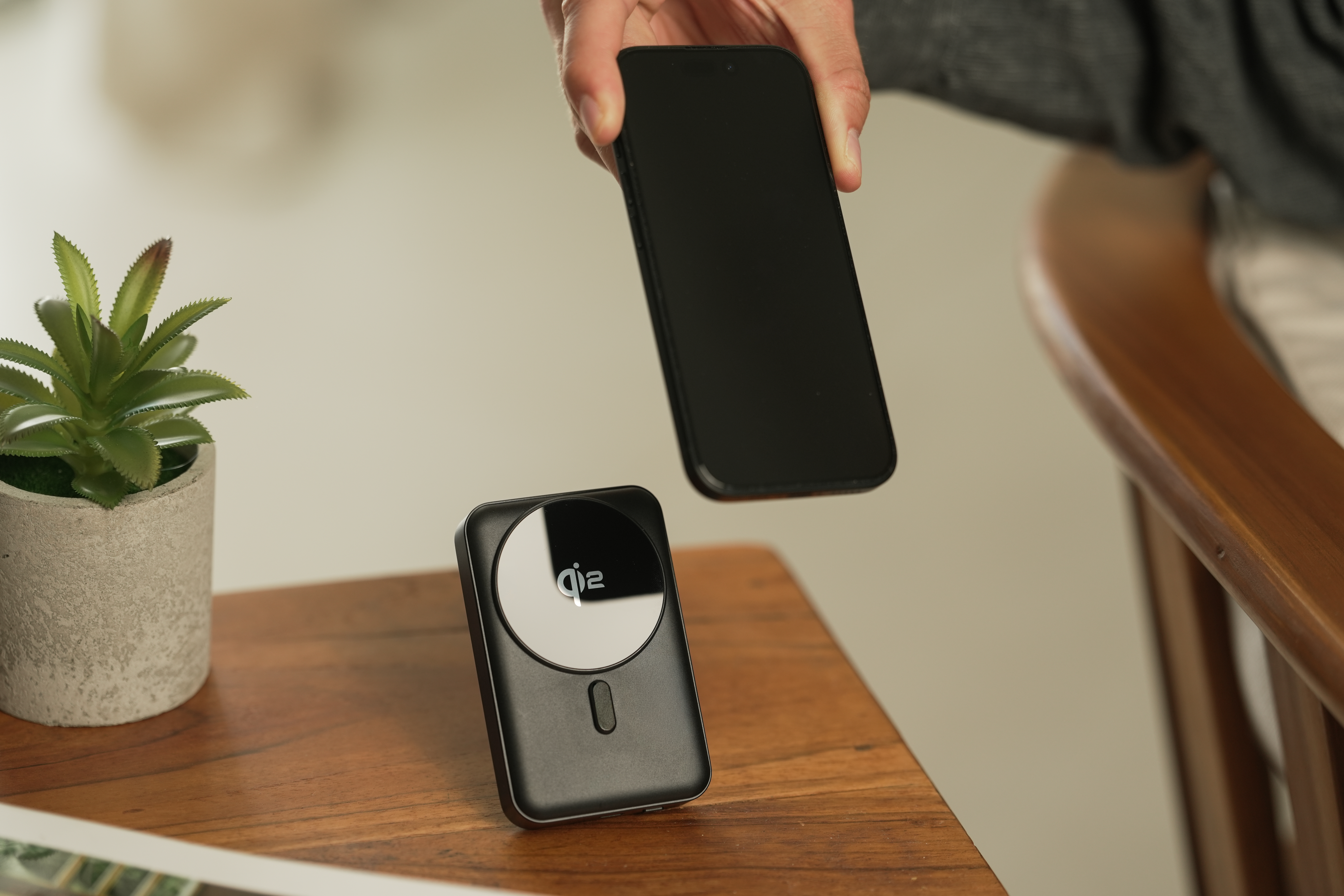 Ein Handy wird über ein schwarzes Ladegerät mit QI-Logo gehalten.