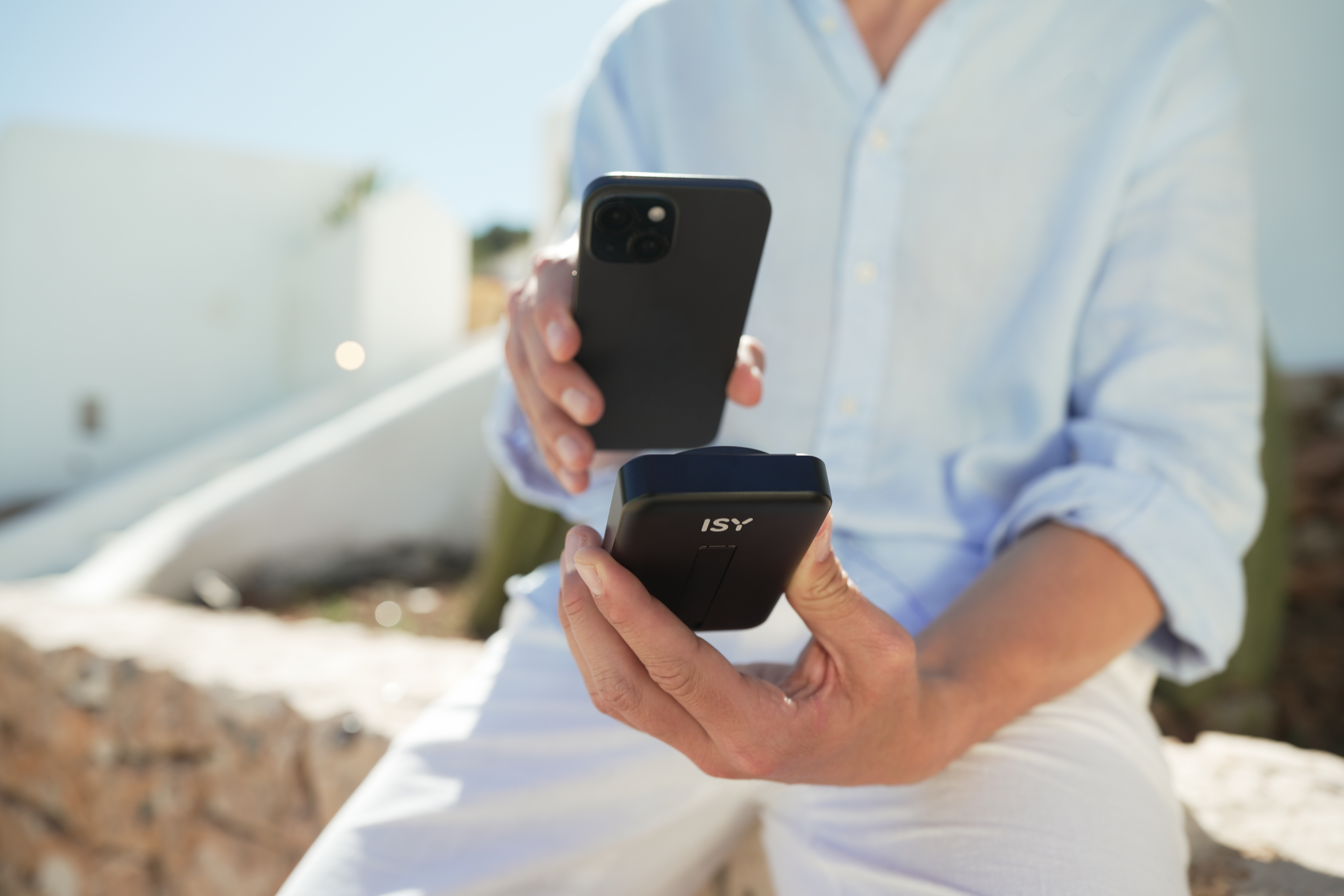 Ein Mann hält ein schwarzes Smartphone und ein schwarzes ISY-Gerät in der Hand.