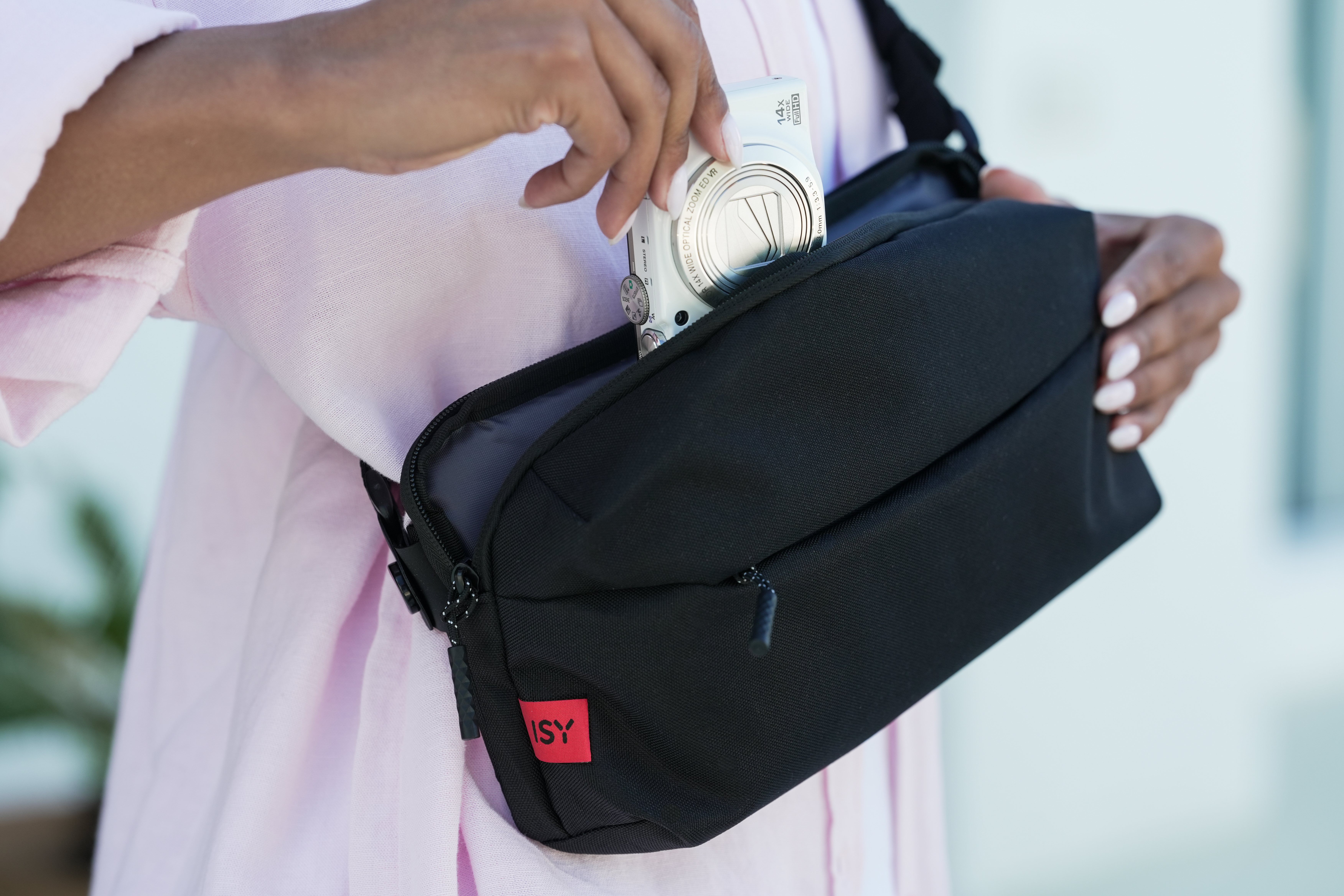 Eine Hand legt eine weiße Kamera in eine schwarze Tasche.