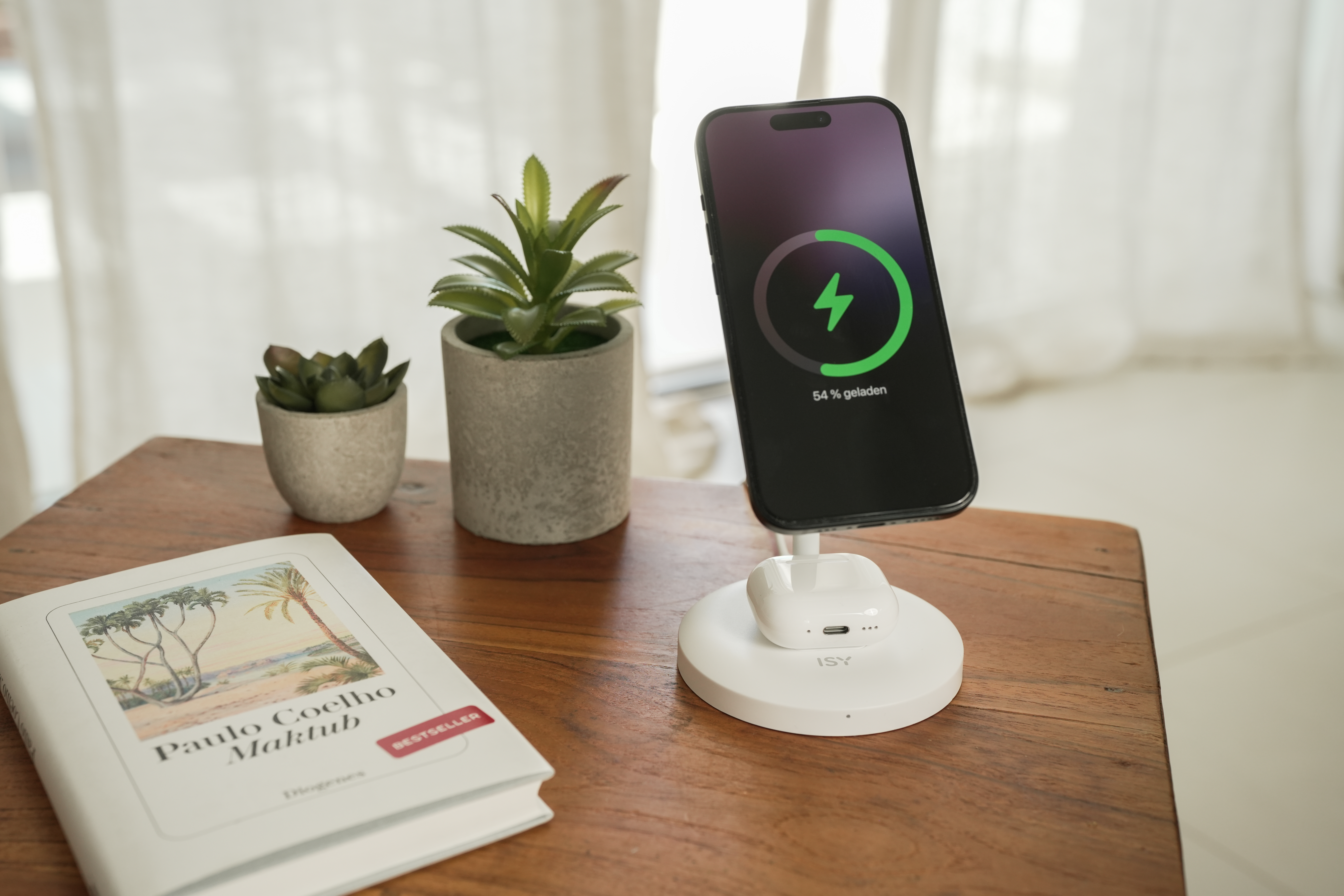Ein Smartphone wird auf einem Ladegerät geladen, daneben ein Buch und Pflanzen.