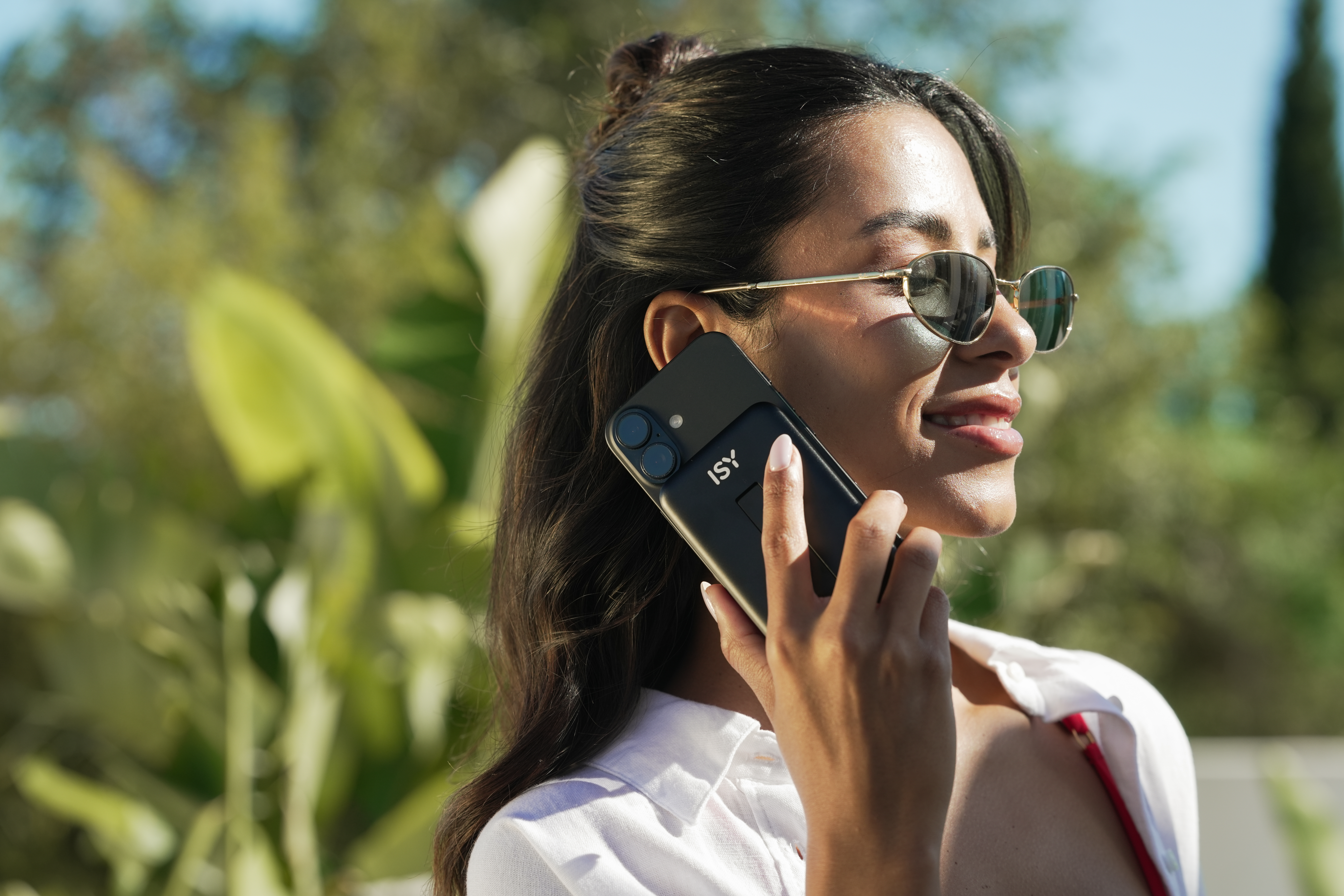 Frau mit Sonnenbrille telefoniert mit einem schwarzen Handy im Freien.