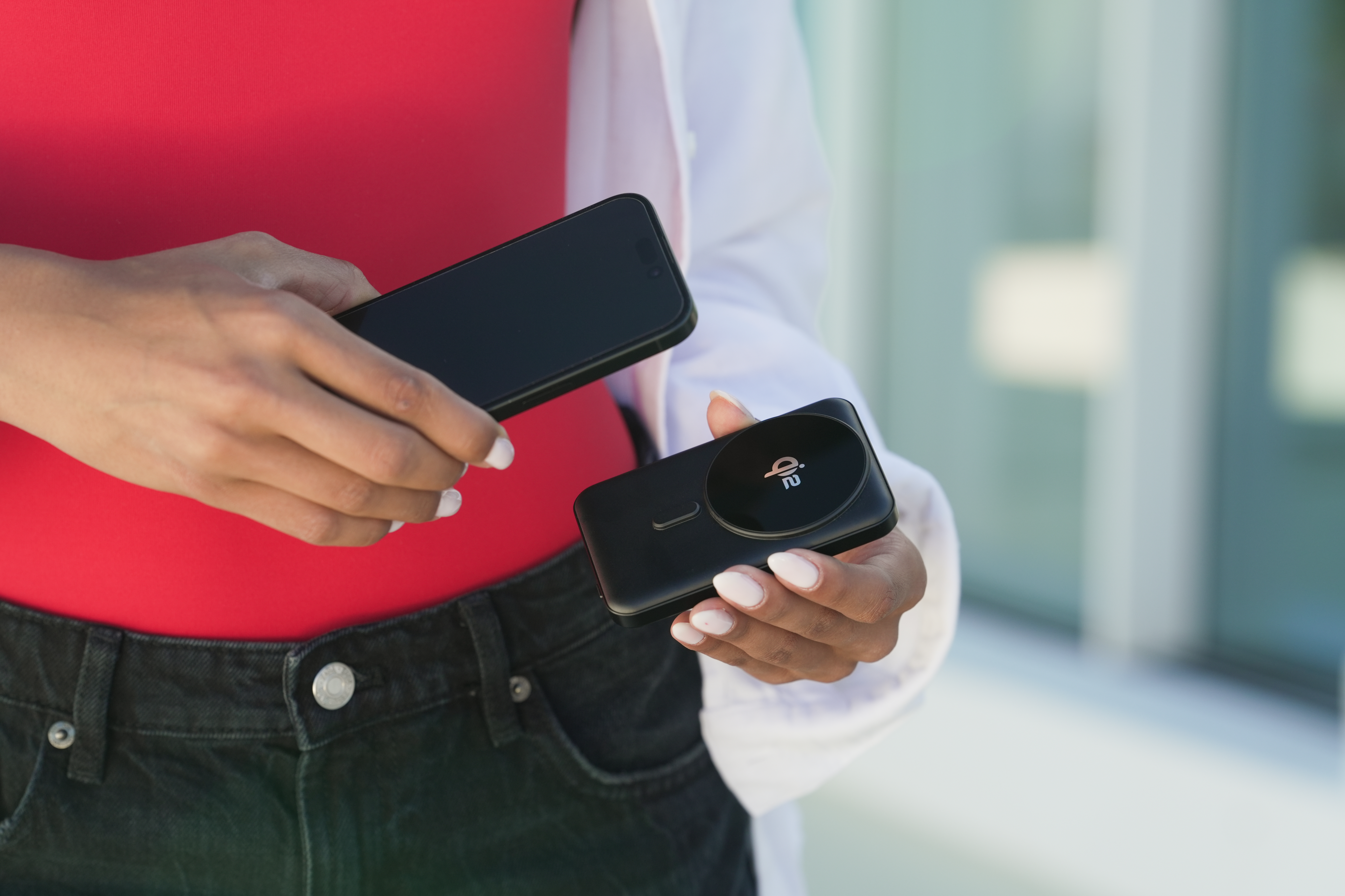 Frau hält ein schwarzes Smartphone und ein schwarzes Ladegerät in der Hand.