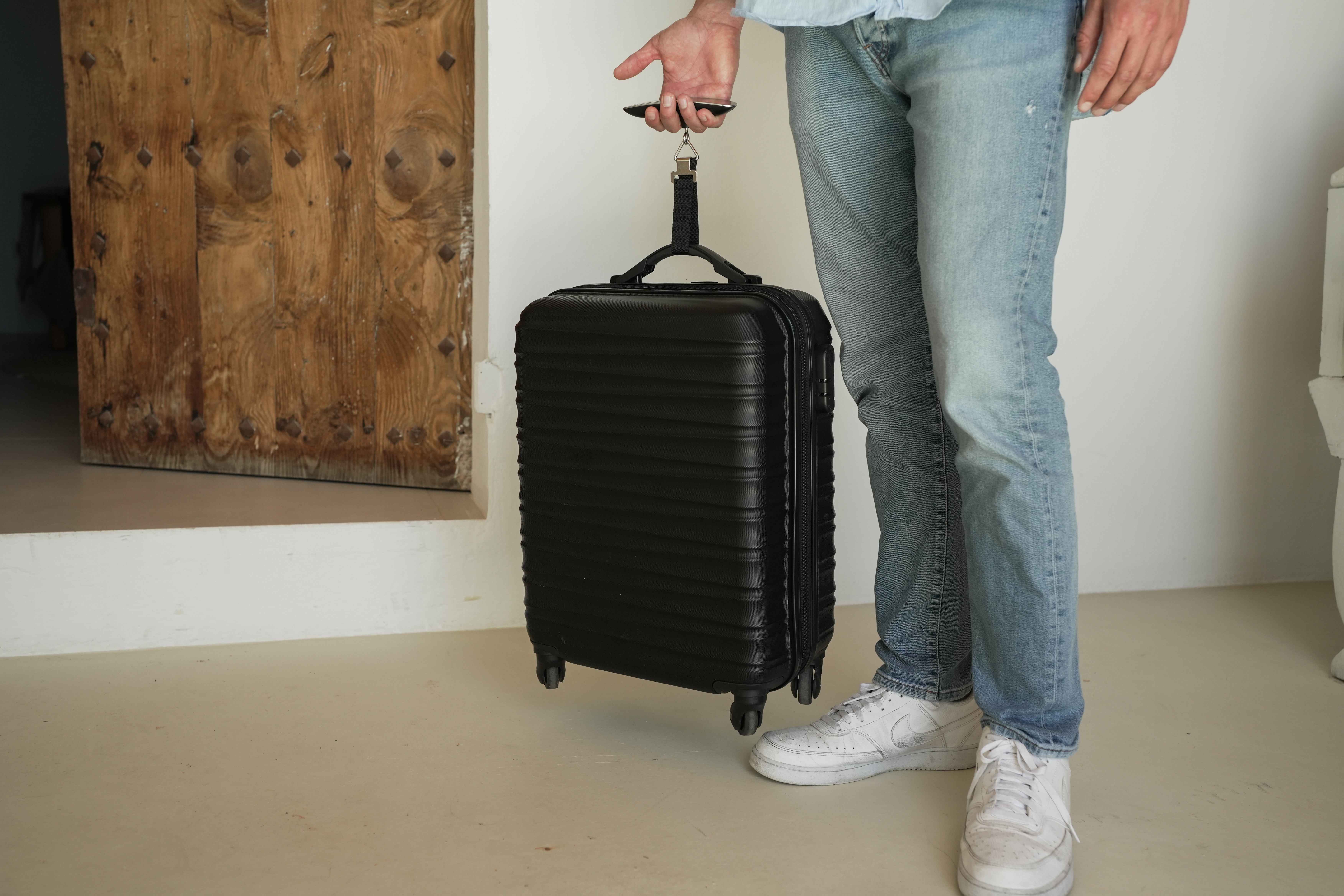 Person mit schwarzem Rollkoffer vor Holztür.