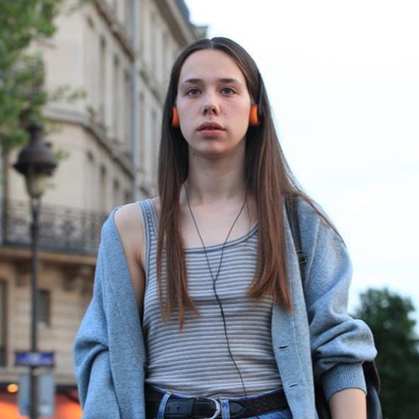 Junge Frau mit Kopfhörern steht vor einem Gebäude in Paris.