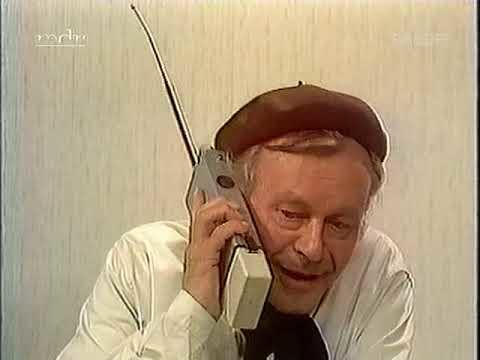 Mann mit braunem Barett telefoniert mit altem Mobiltelefon vor gemustertem Hintergrund.