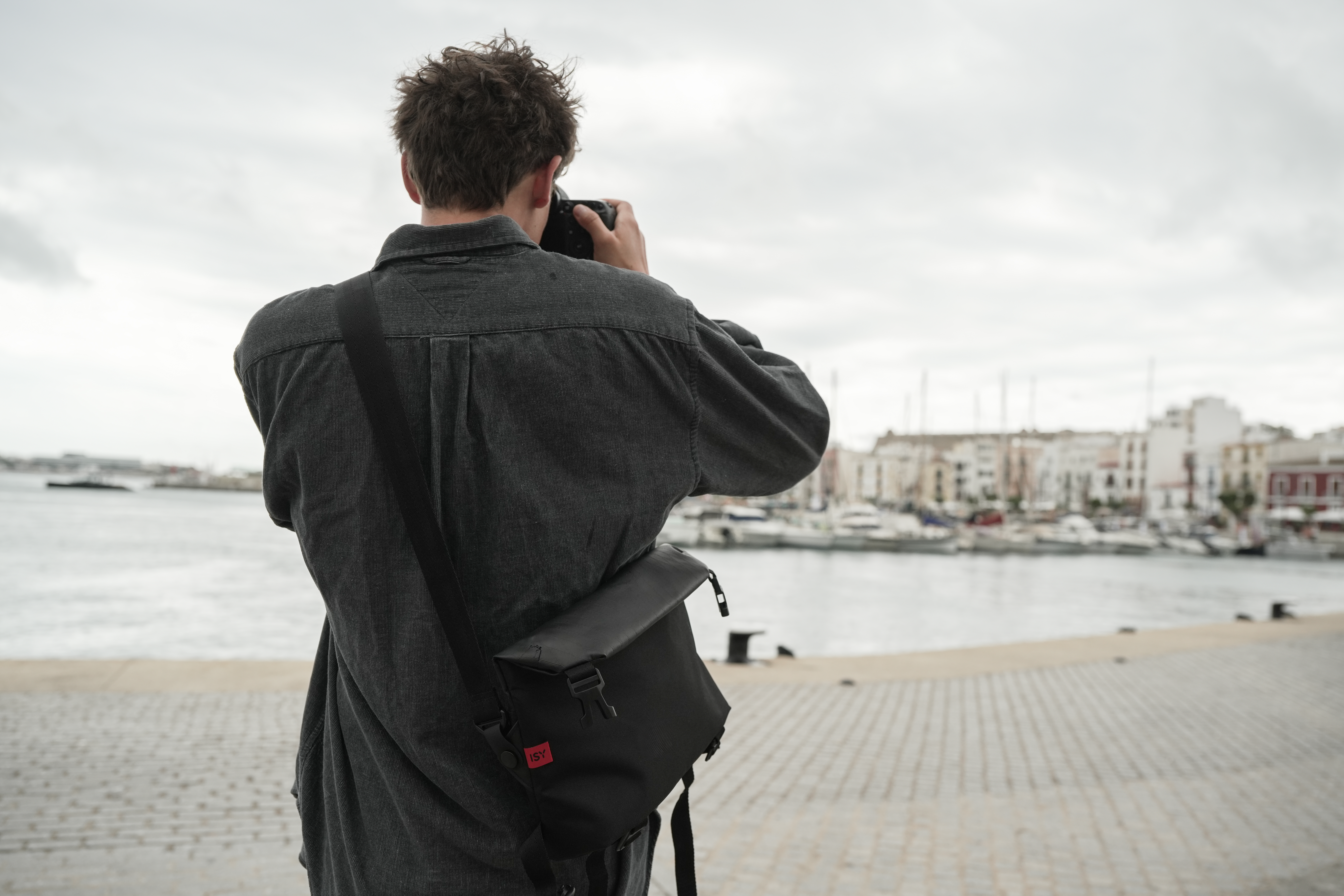 Mann fotografiert am Hafen mit Stadtkulisse im Hintergrund.