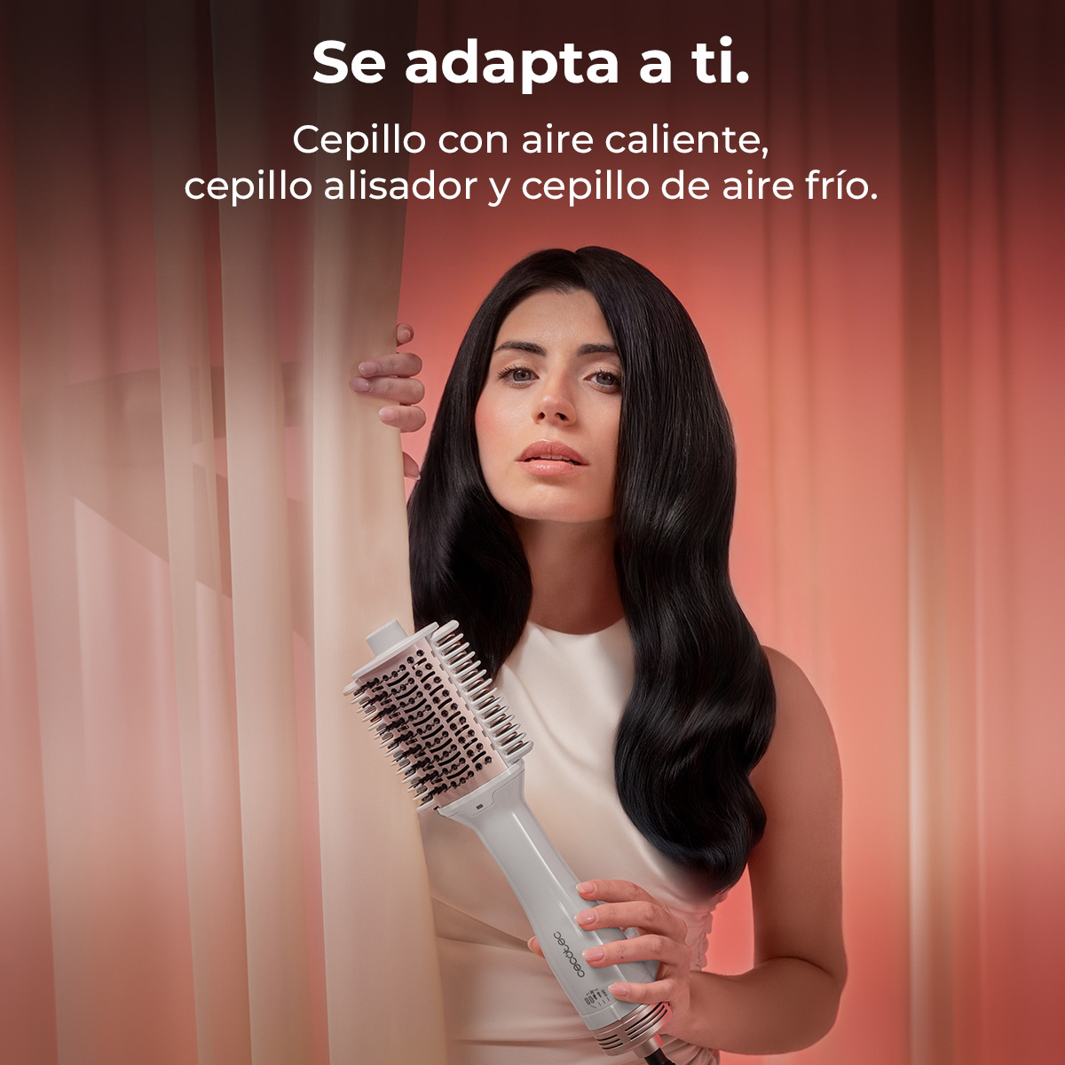 Una mujer sostiene un cepillo secador blanco sobre fondo rosa.