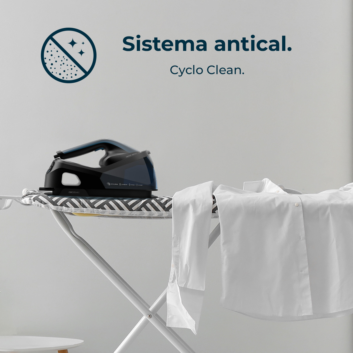 Una plancha de vapor negra descansa sobre una tabla de planchar junto a camisas blancas.