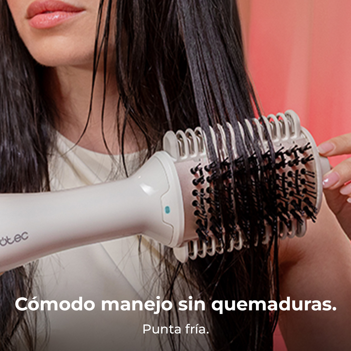 Una mujer se seca el pelo largo y oscuro con un cepillo secador blanco.