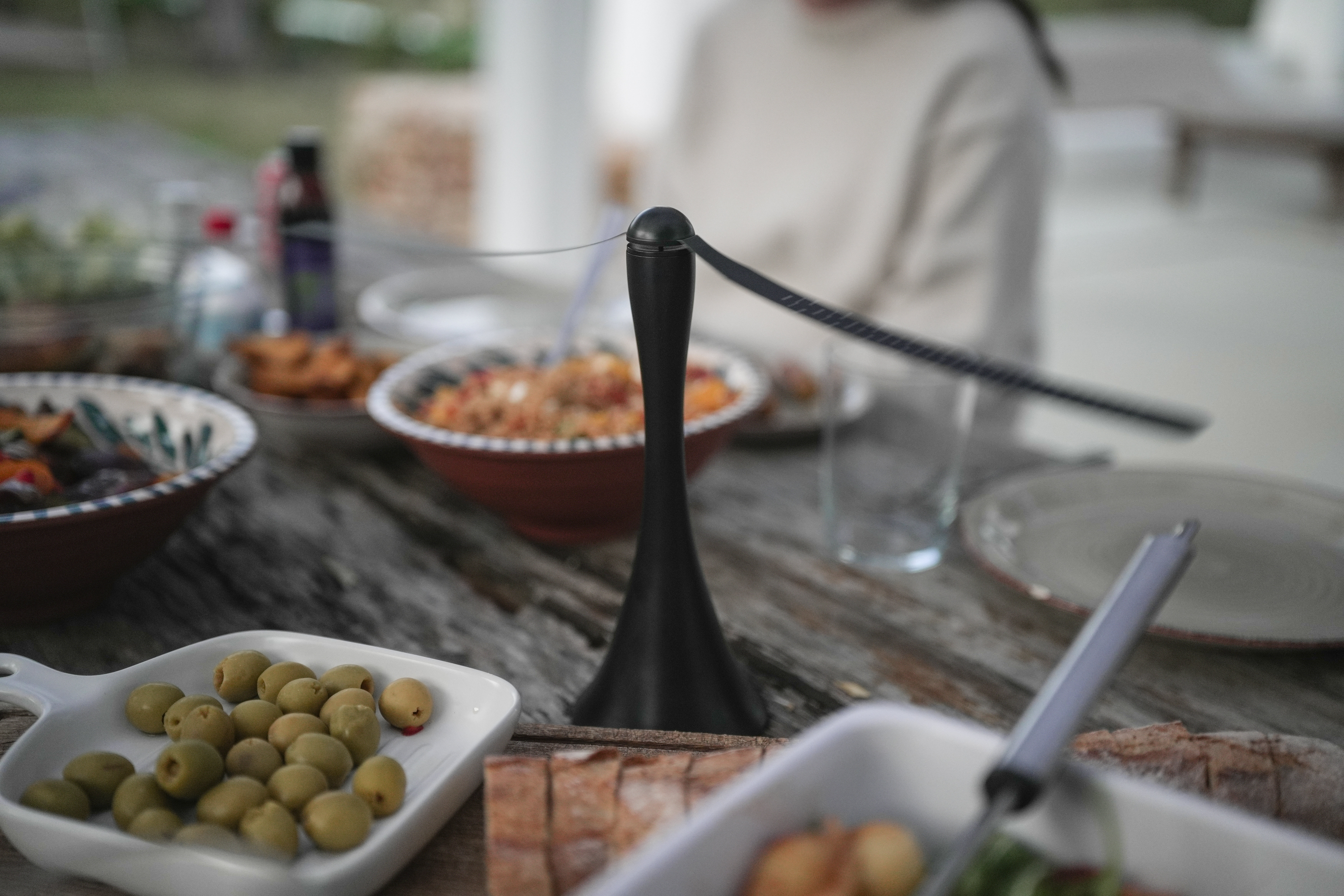 Tisch mit Oliven, Brot und Essen, im Hintergrund eine Person.