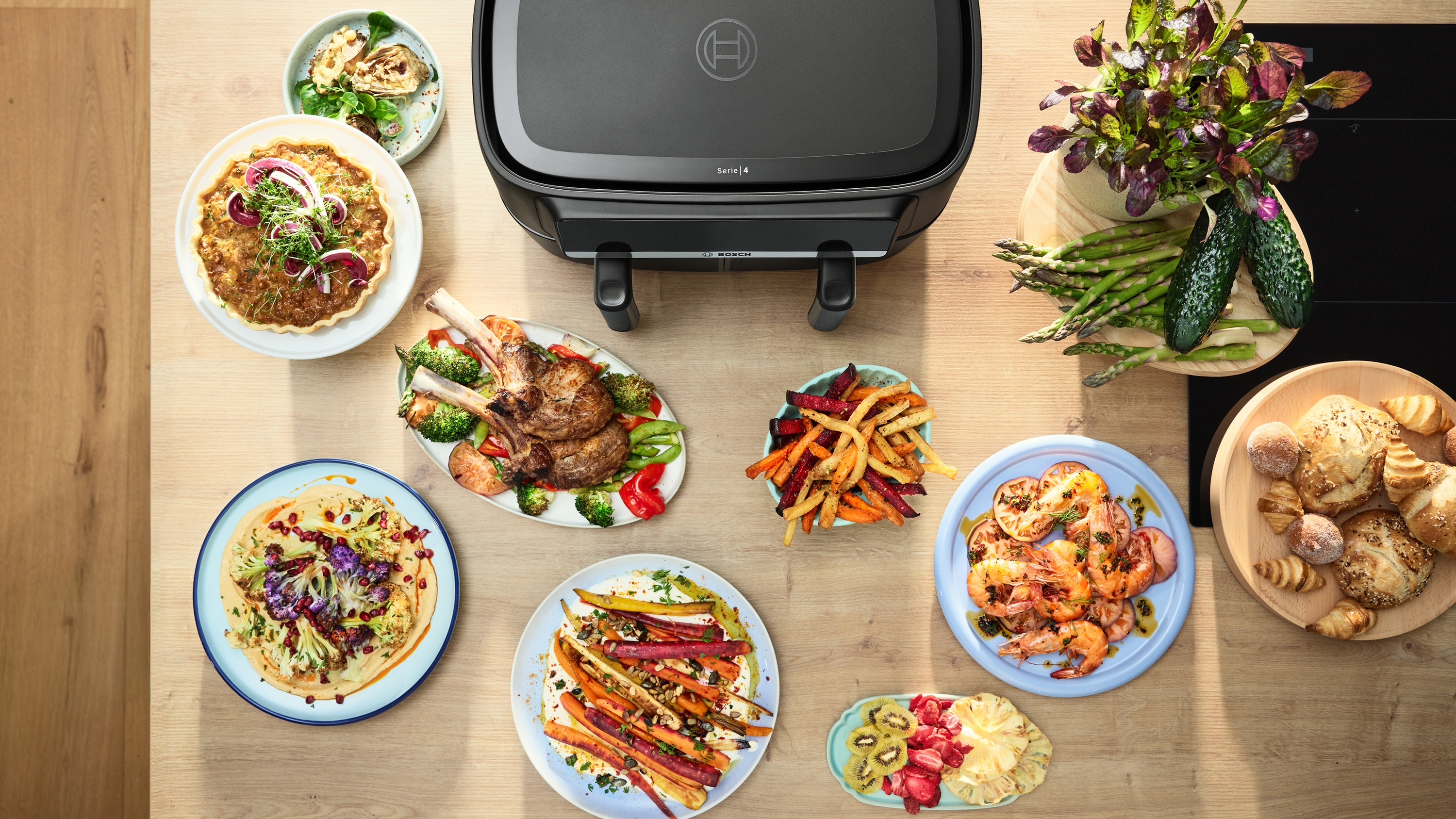 Eine Tischansicht mit einer schwarzen Bosch-Grillplatte, umgeben von verschiedenen Speisen.