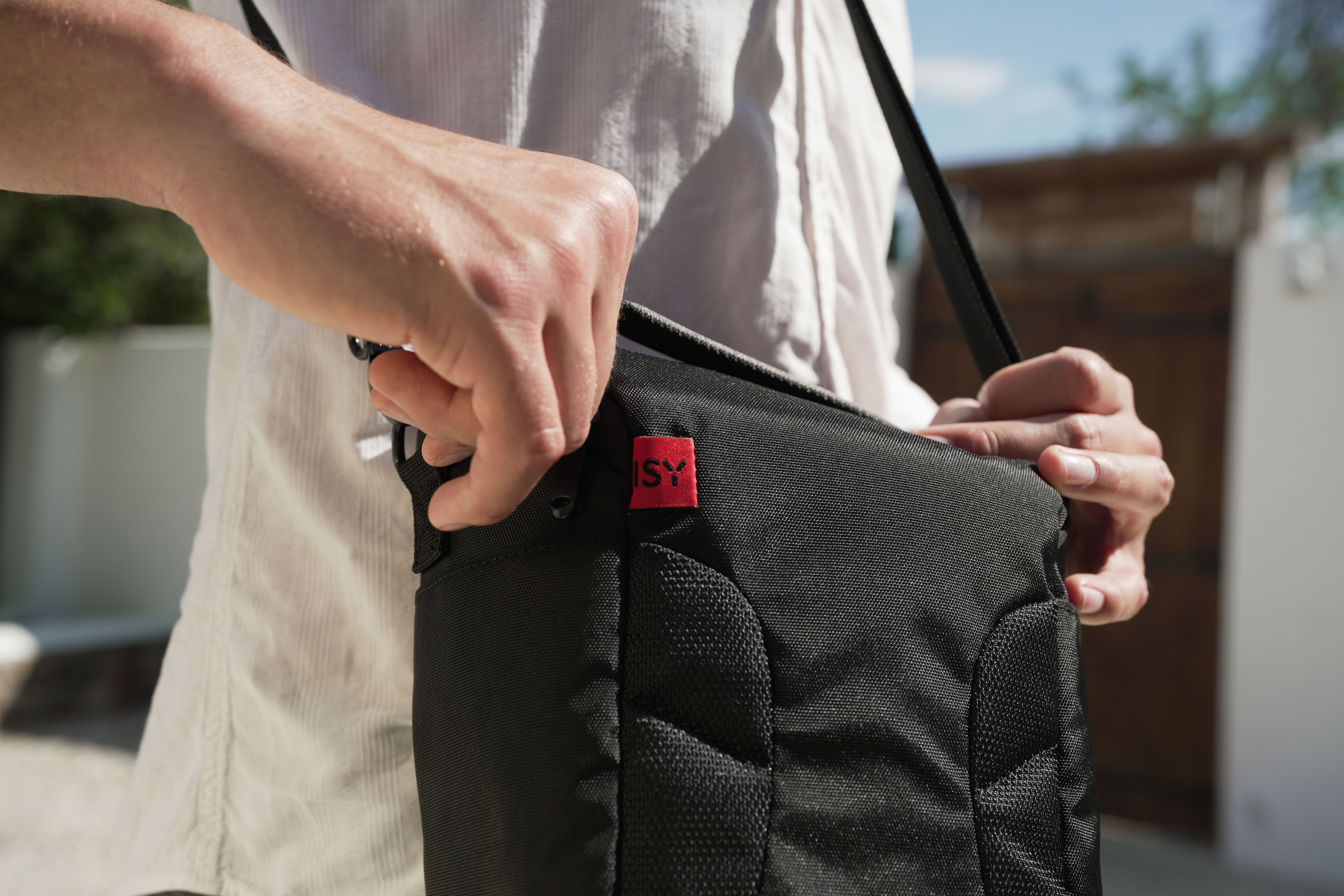 Eine Hand schließt eine schwarze Tasche mit rotem 