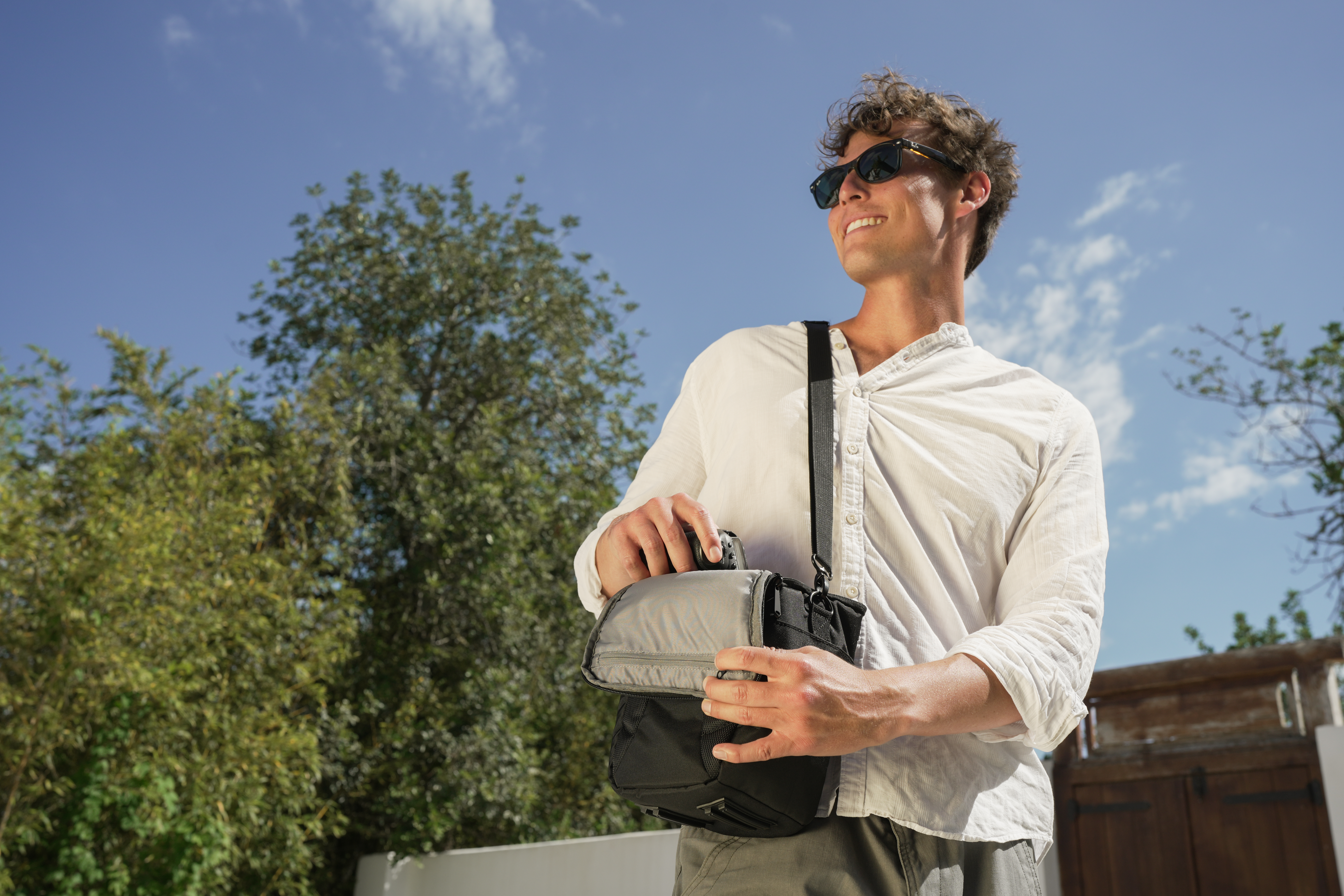 Ein Mann mit Sonnenbrille packt eine Kameratasche aus. Er trägt ein weißes Hemd.
