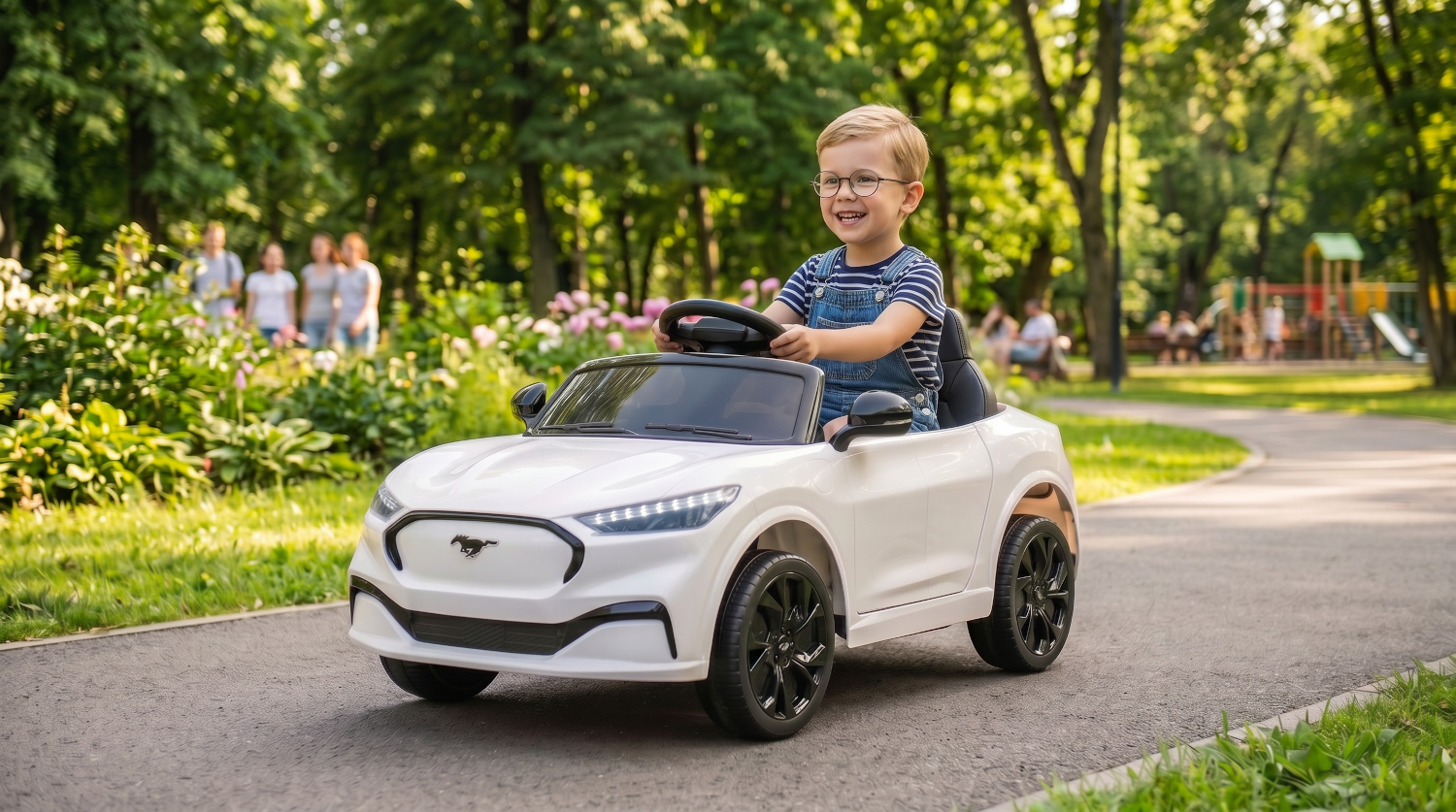 A boy drives a white electric car in a park, with trees and a playground in the background.