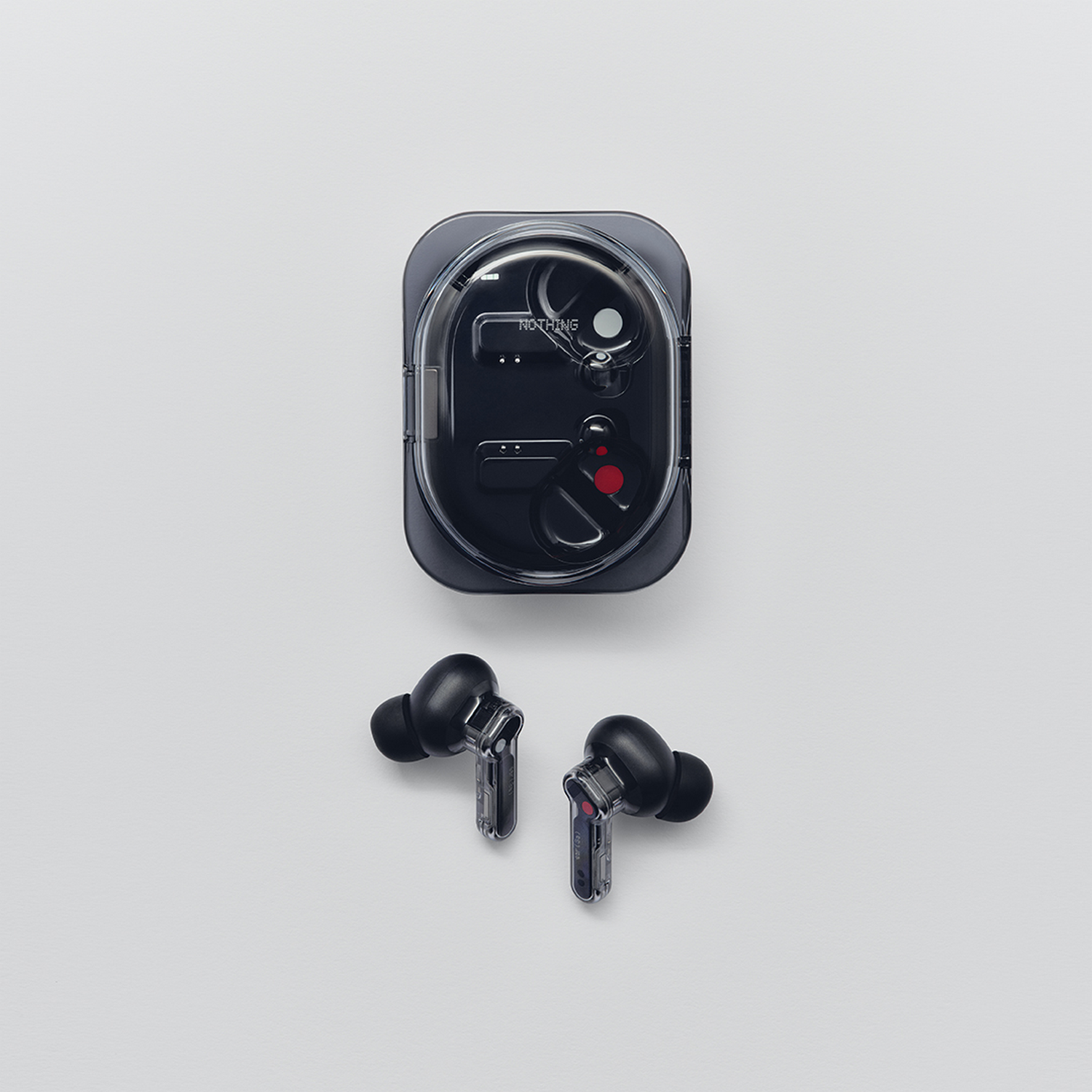 Auriculares inalámbricos negros con tallo transparente junto a su estuche de carga sobre fondo blanco.