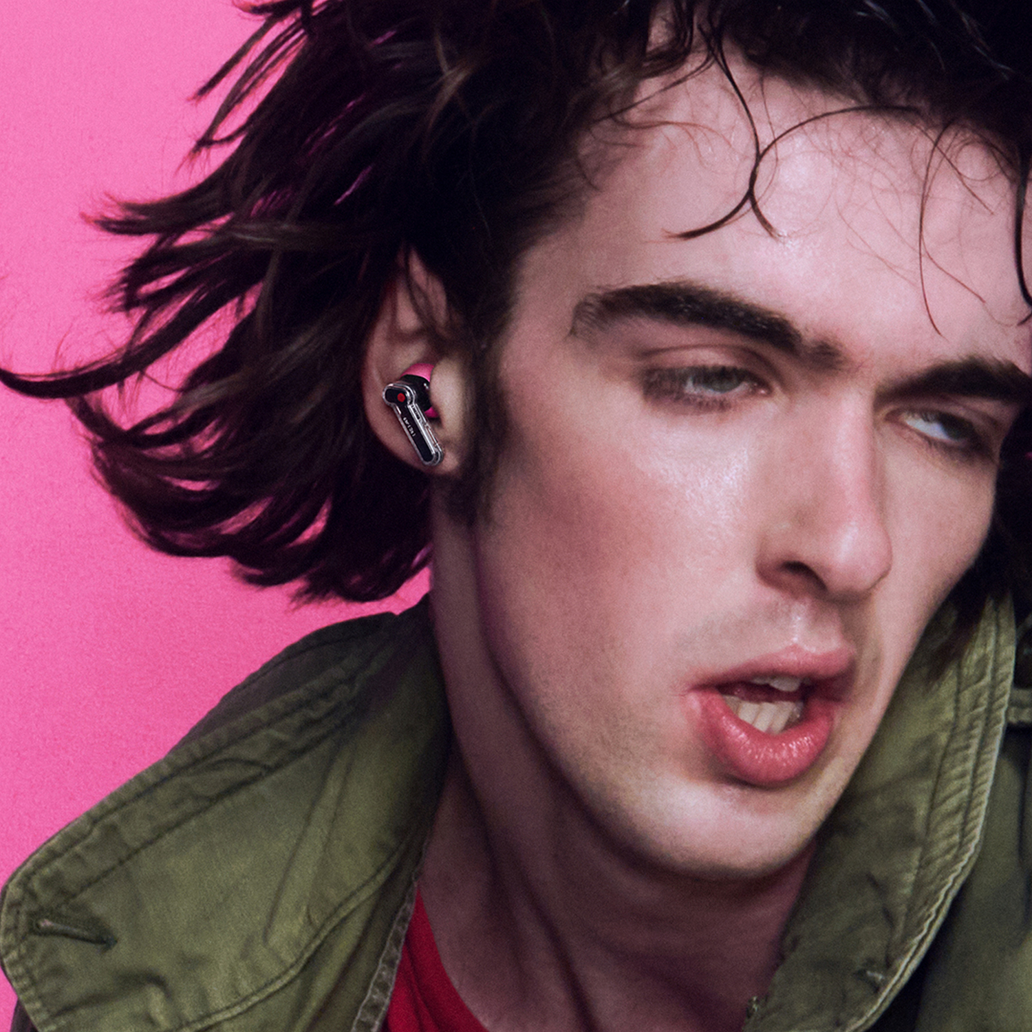 Hombre con audífono sobre fondo rosa, con chaqueta verde.