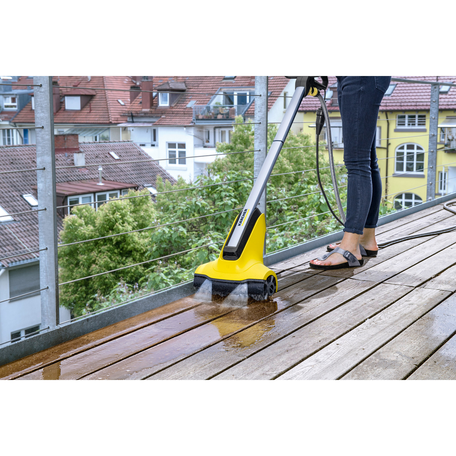 Persona che pulisce un ponte di legno con un dispositivo Kärcher giallo.