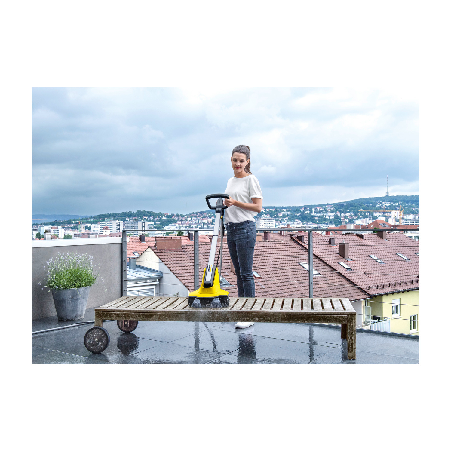 Donna pulisce panca di legno su terrazzo con pulitore Karcher, vista città.