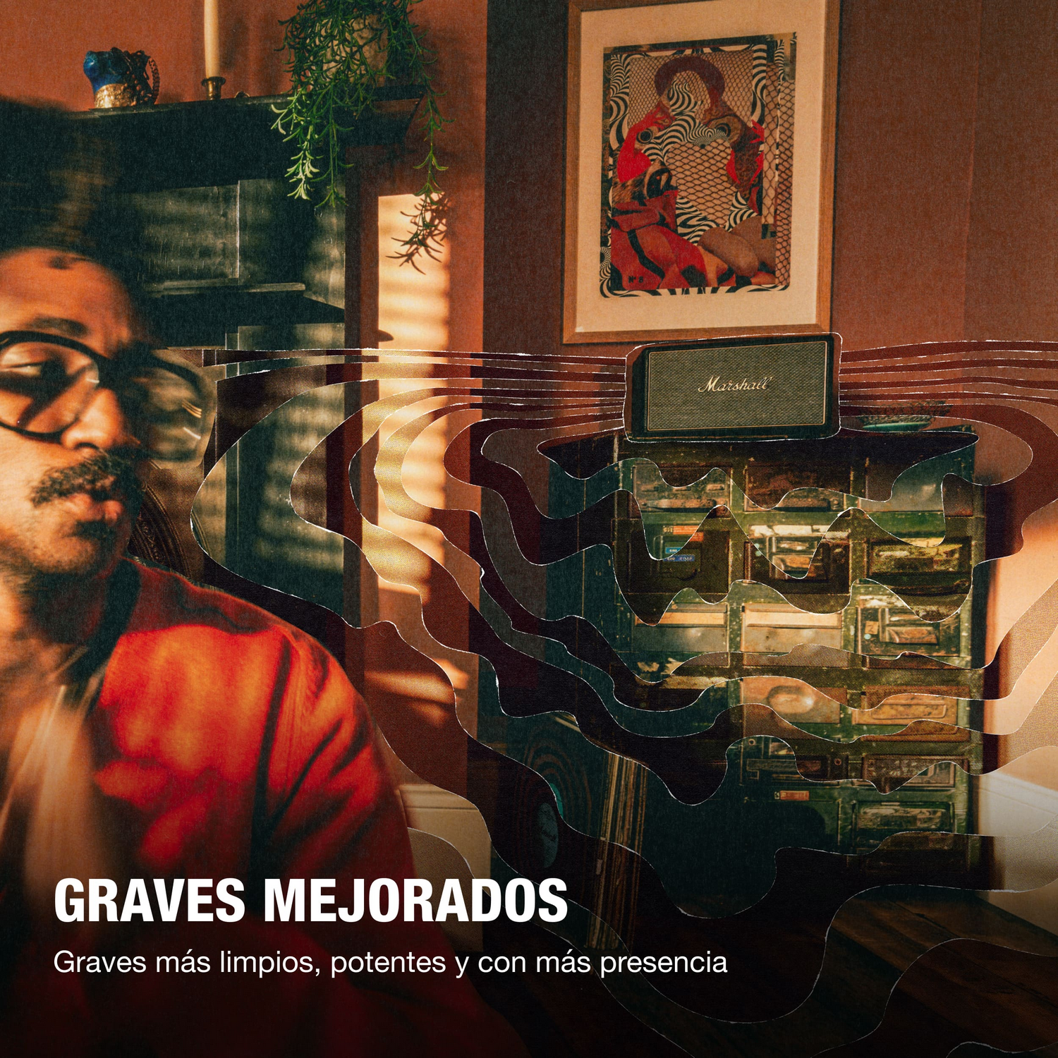 Hombre con gafas frente a un estante con altavoz Marshall y obra de arte.