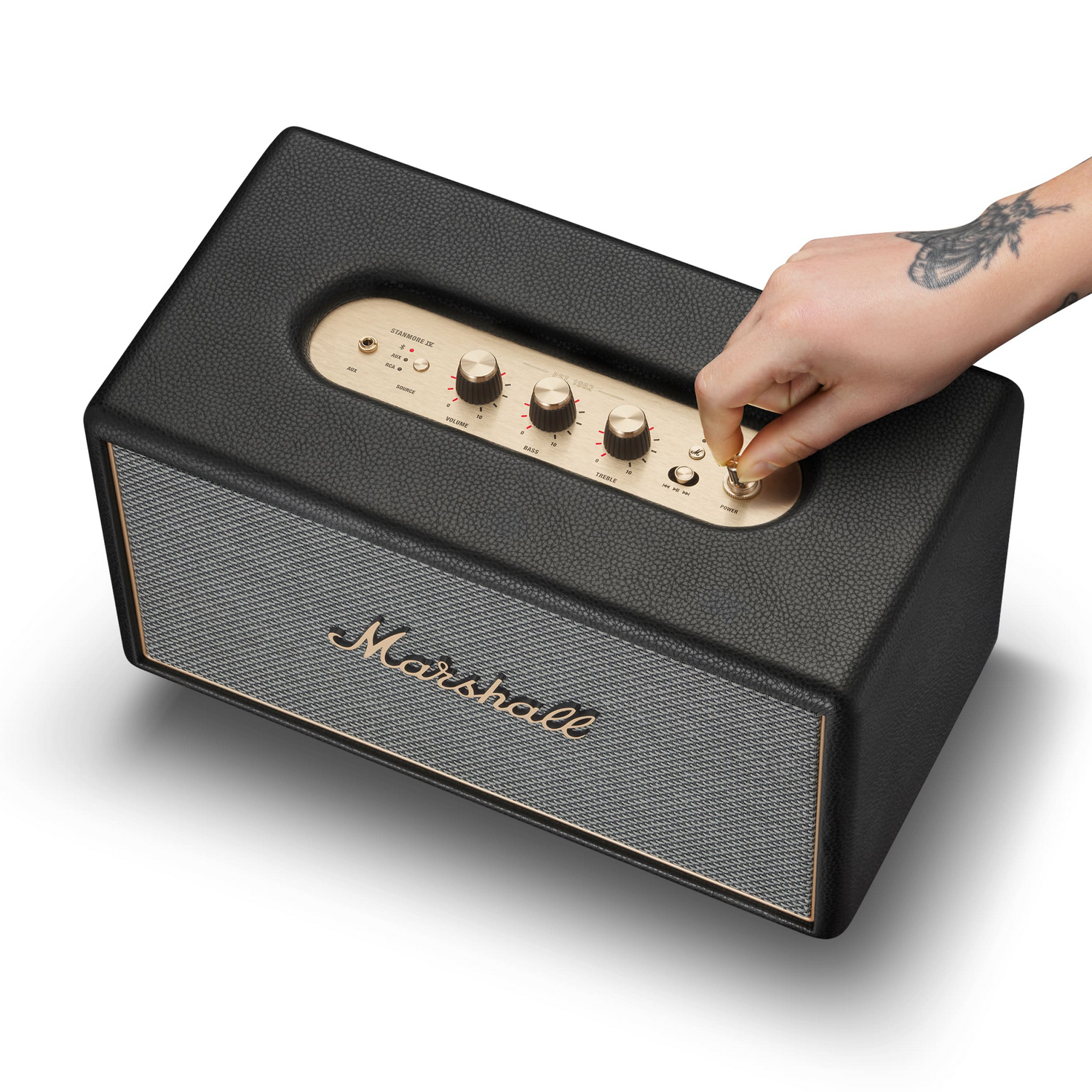 Una mano tatuada gira la perilla dorada de un altavoz Marshall negro.