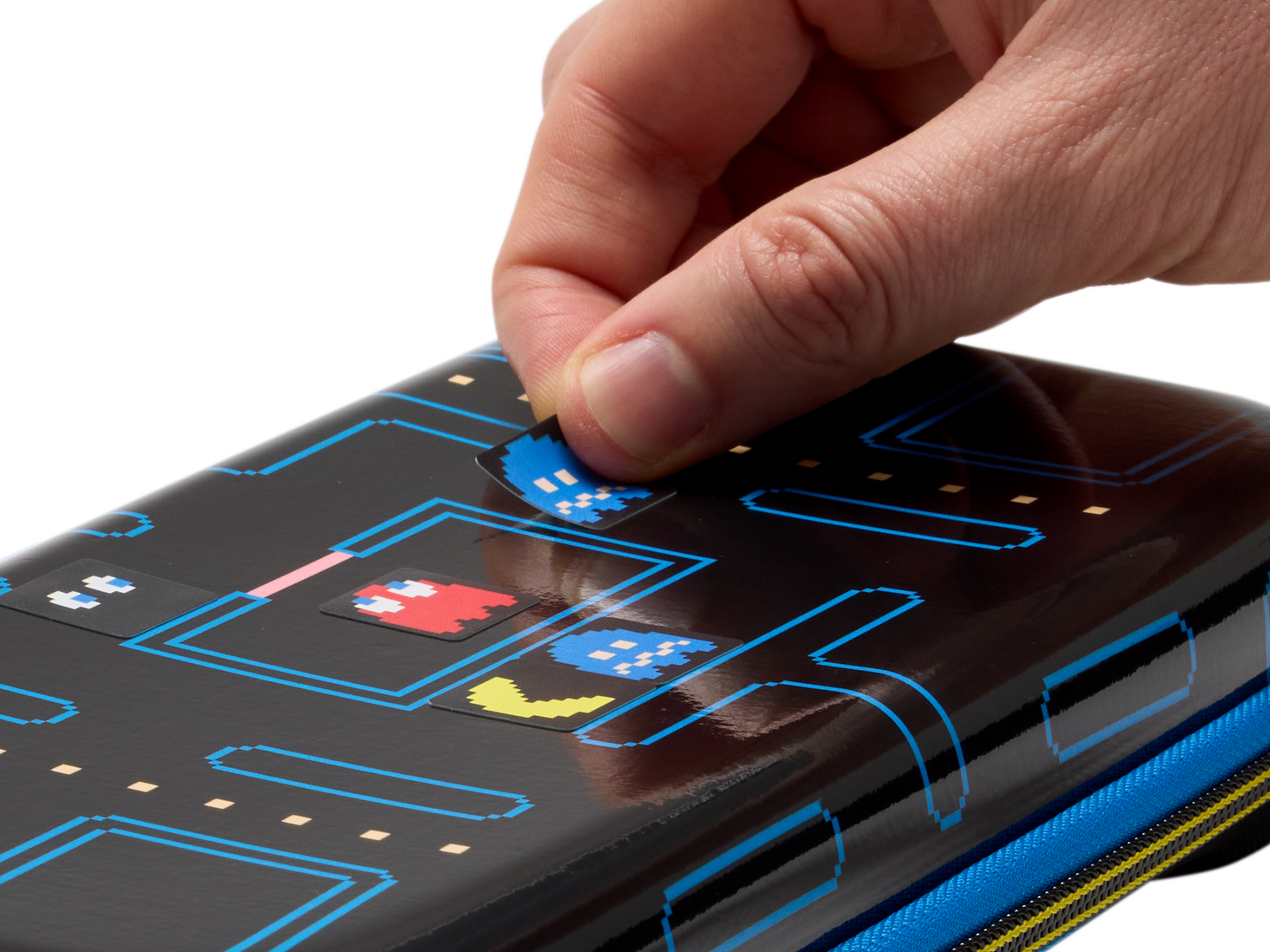 Ein Finger klebt einen Pac-Man-Geist-Aufkleber auf eine schwarze Hülle mit Pac-Man-Motiv.