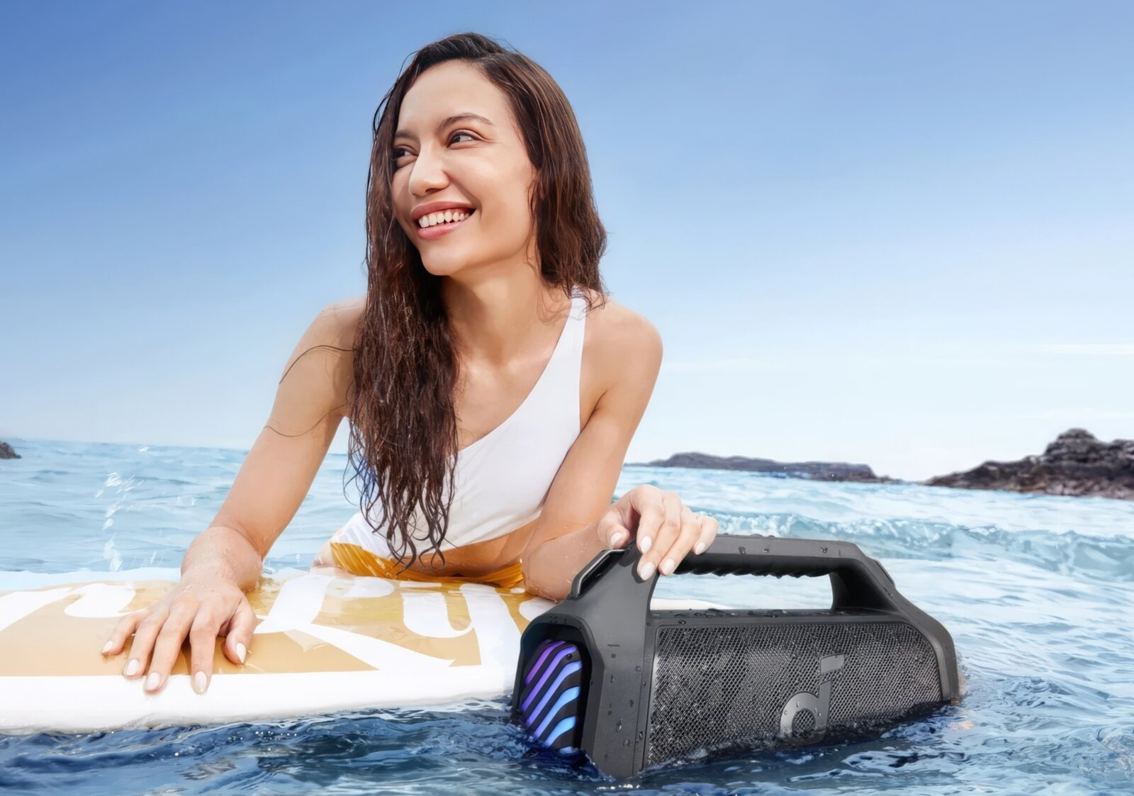 Kobieta z deską surfingową i głośnikiem w morzu, błękitne niebo.
