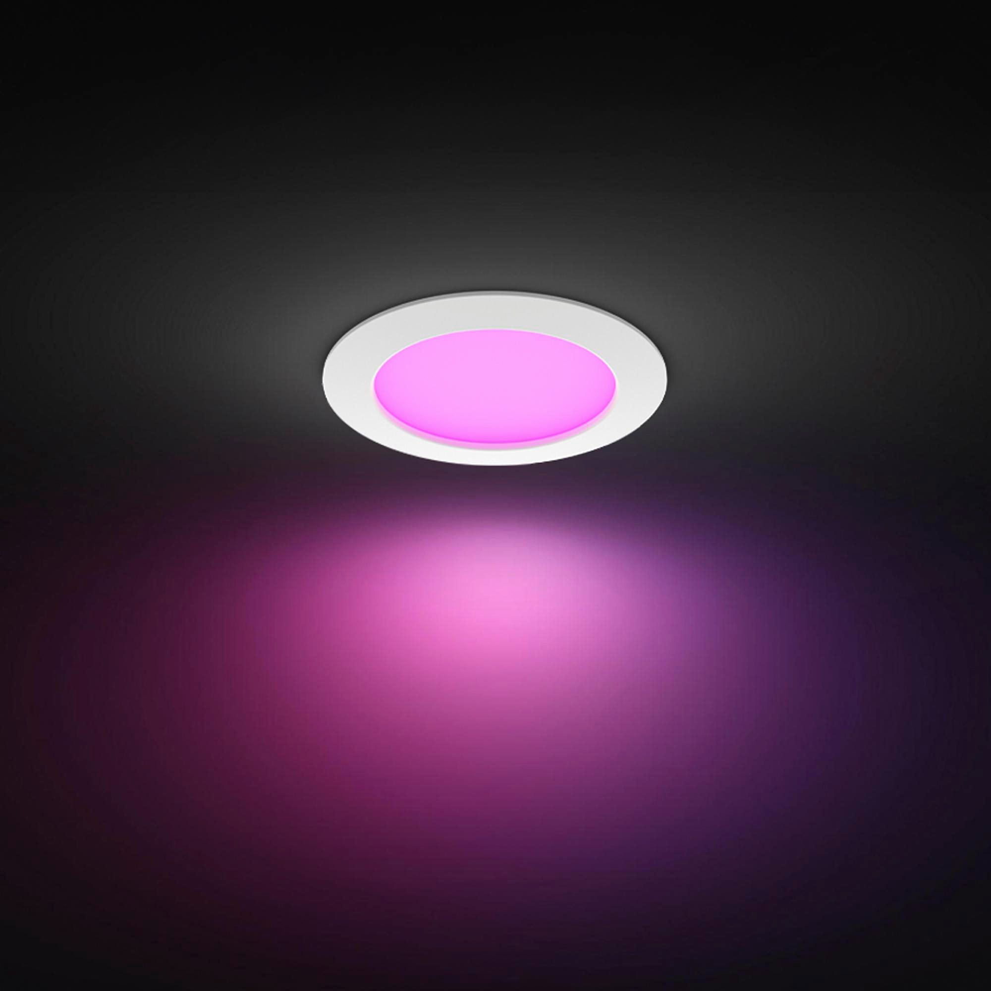 Eine runde Deckenleuchte strahlt pinkes Licht auf eine dunkle Wand.