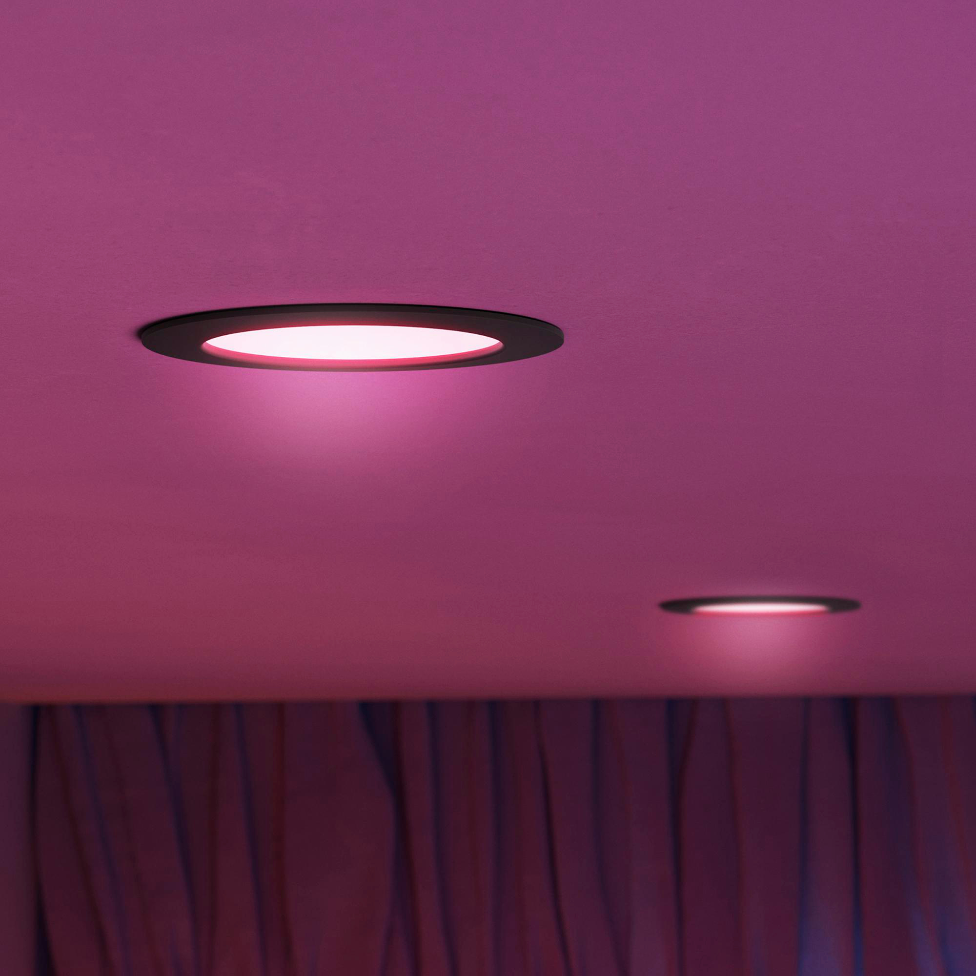 Zwei runde Einbaustrahler leuchten auf einer rosa Decke über lila Vorhängen.